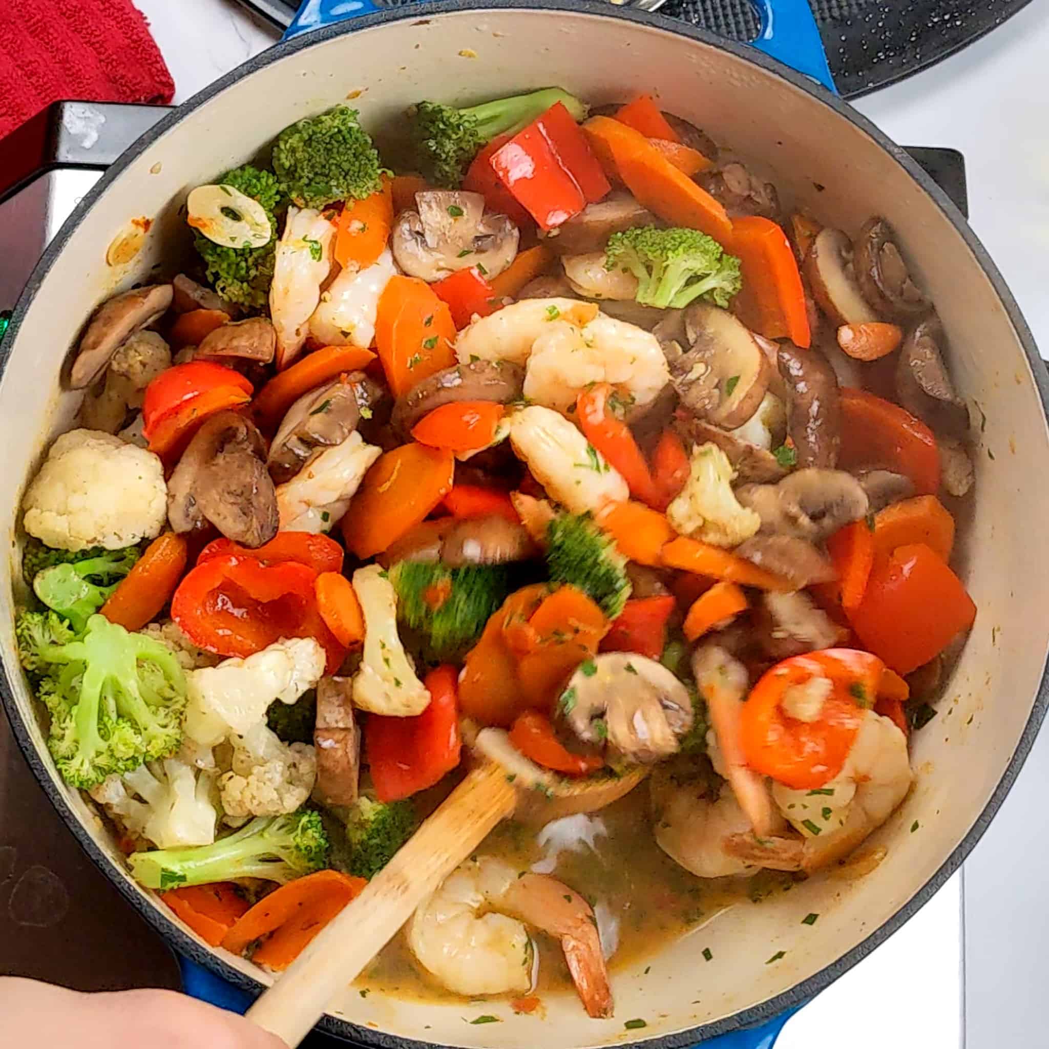 vegetables and shrimp being mixed with a wooden spoon in a dutch oven