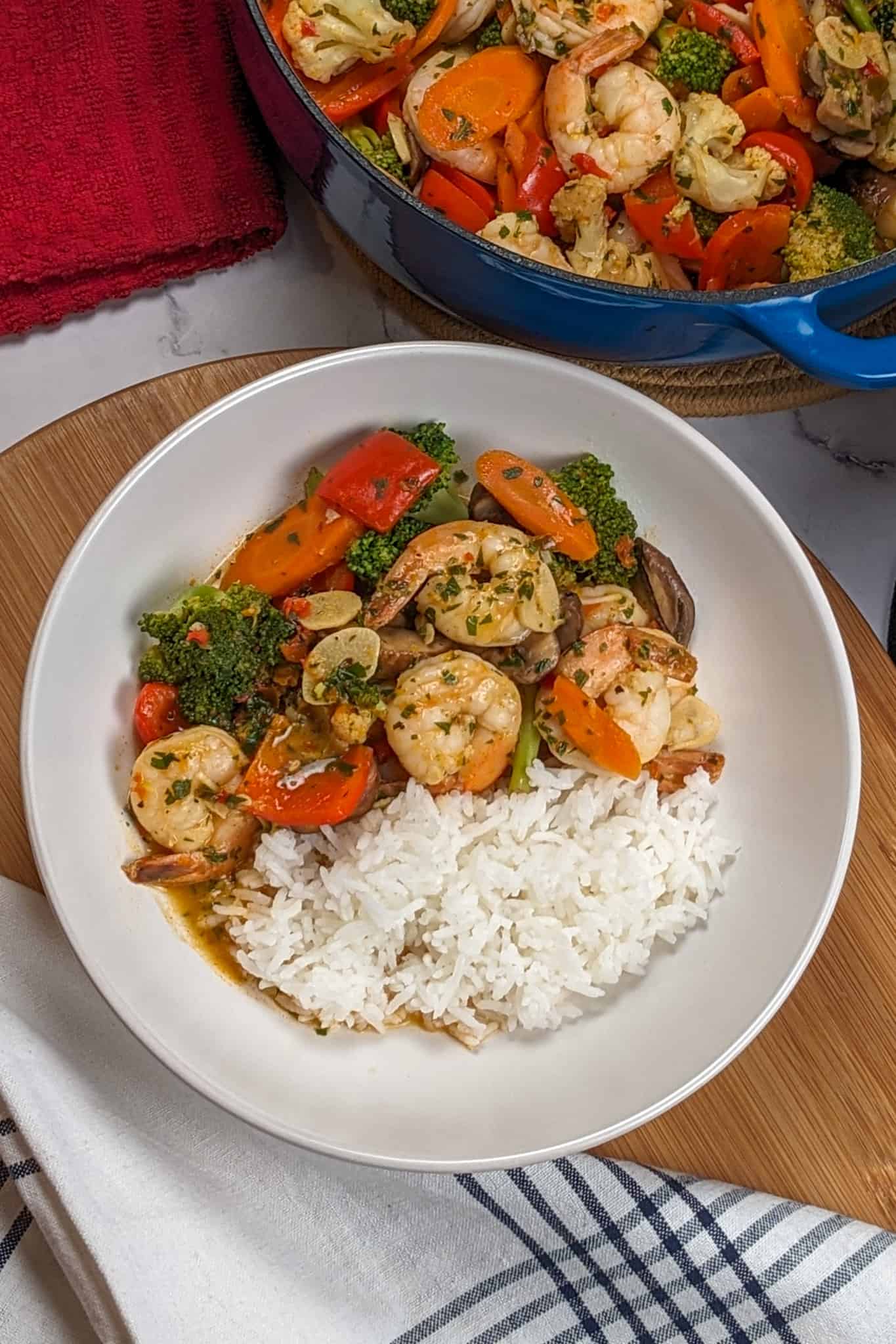 top of the Best Spicy Sauteed Chili Lemon Garlic Shrimp and Vegetables dish on a wooden lazy susan next to kitchen top and dutch of with the shrimp and vegetables