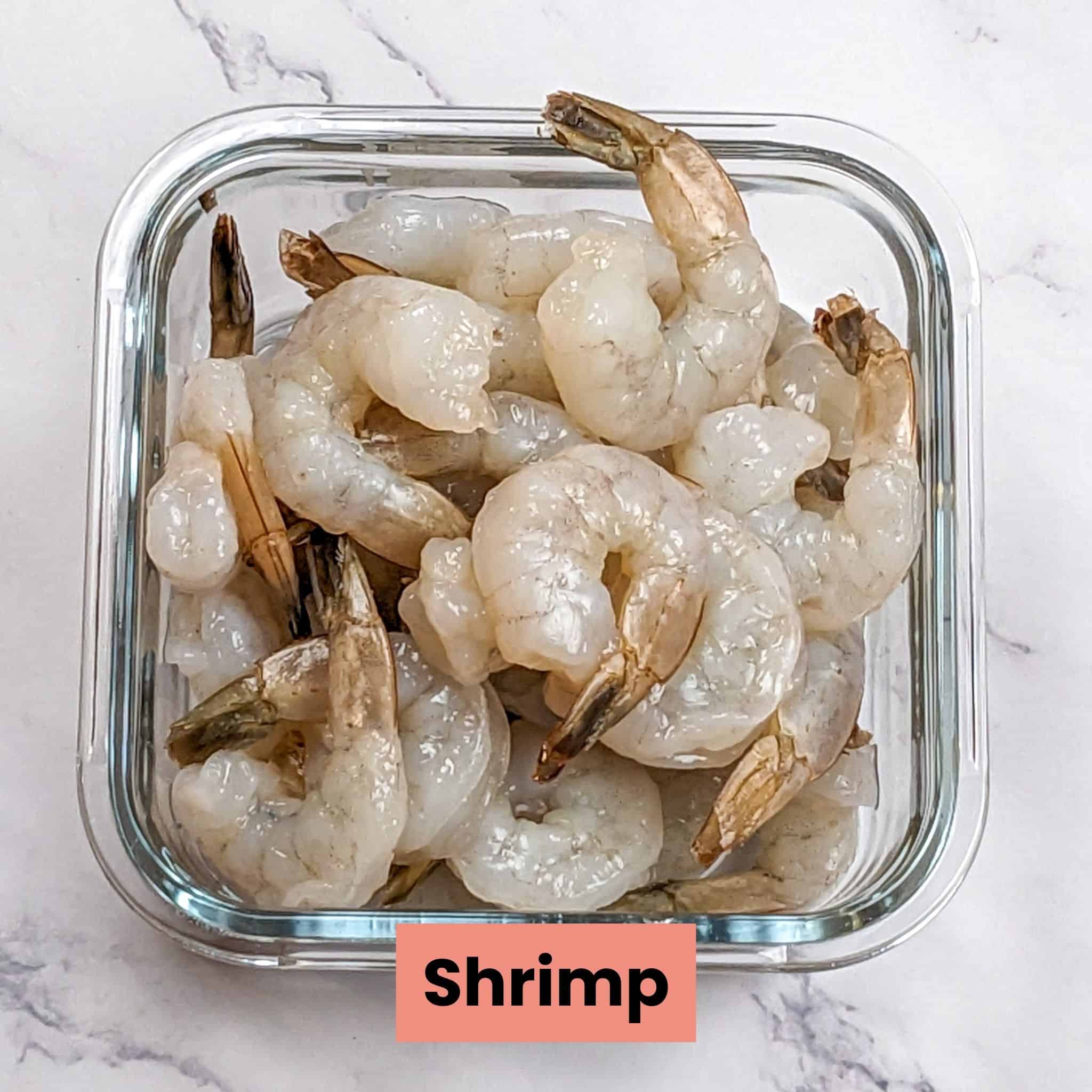 raw tail-on shrimp in a glass square clear dish