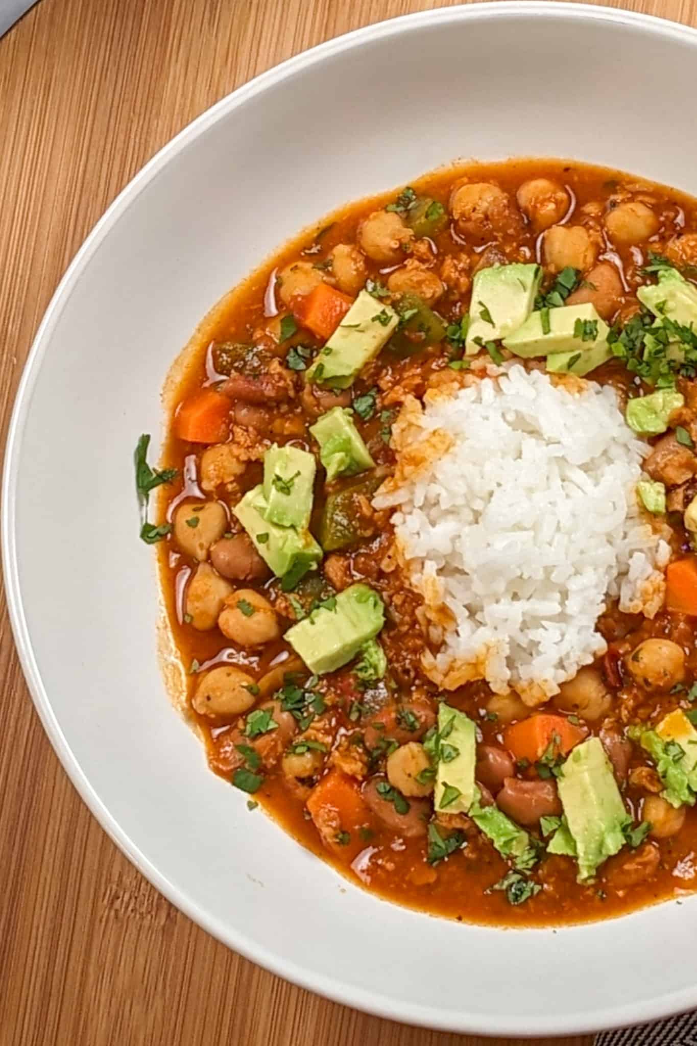 top view of the Vegetarian Smoky Chipotle Chorizo and Bean Stew surrounding cooked rice in a wide rim bowl