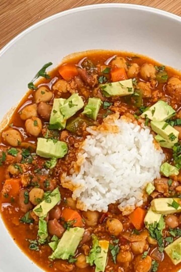 top view of the Vegetarian Smoky Chipotle Chorizo and Bean Stew surrounding cooked rice in a wide rim bowl