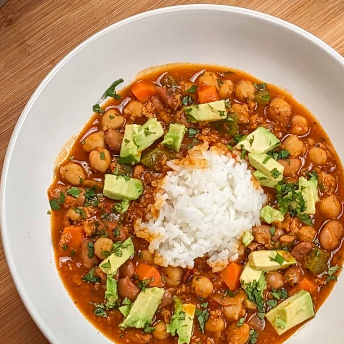 top view of the Vegetarian Smoky Chipotle Chorizo and Bean Stew surrounding cooked rice in a wide rim bowl
