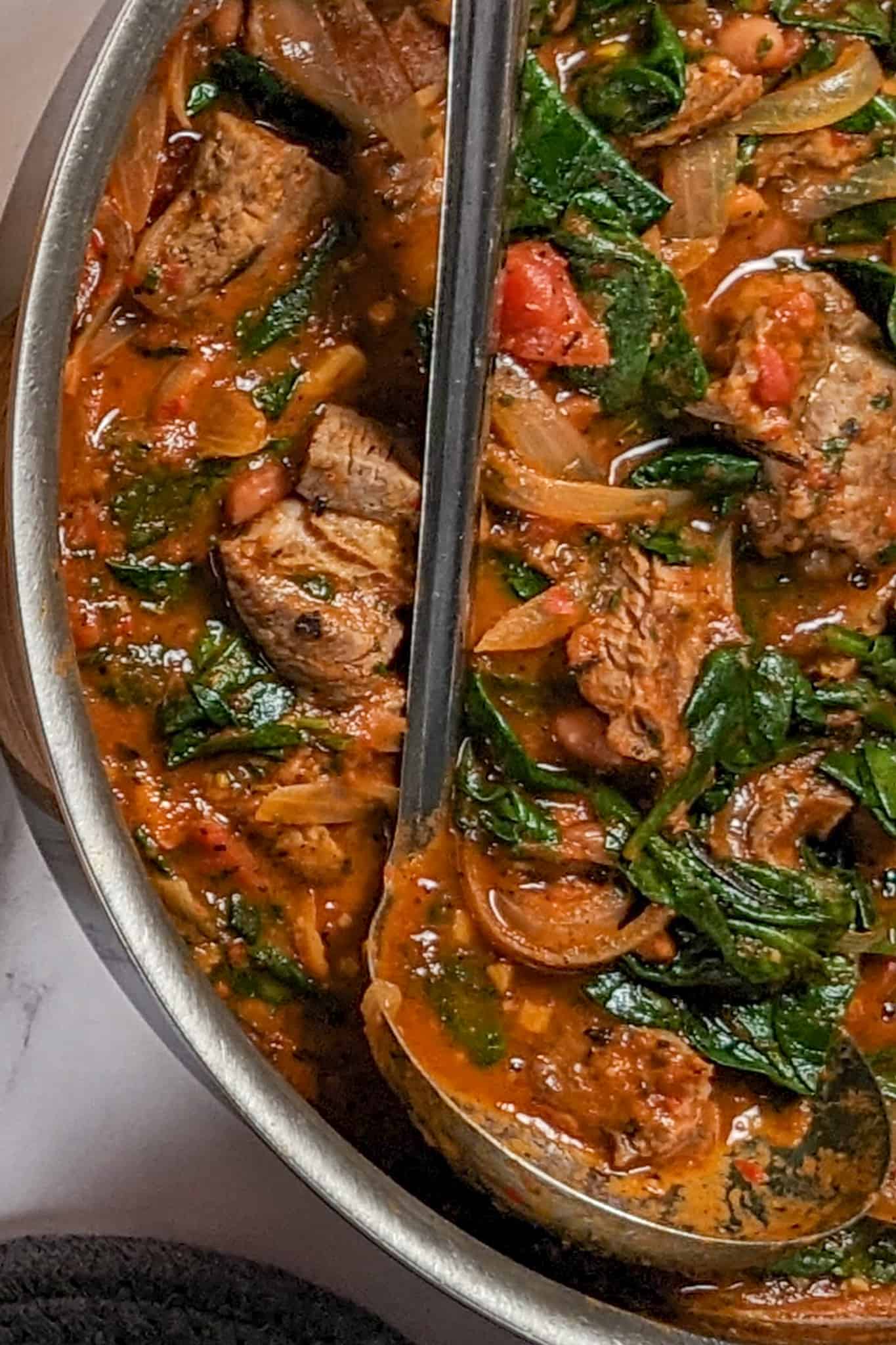 top view of the Baharat Spiced Bean and Lamb Stew in the all-clad stainless steel saute pan wtih a stainless steel ladle