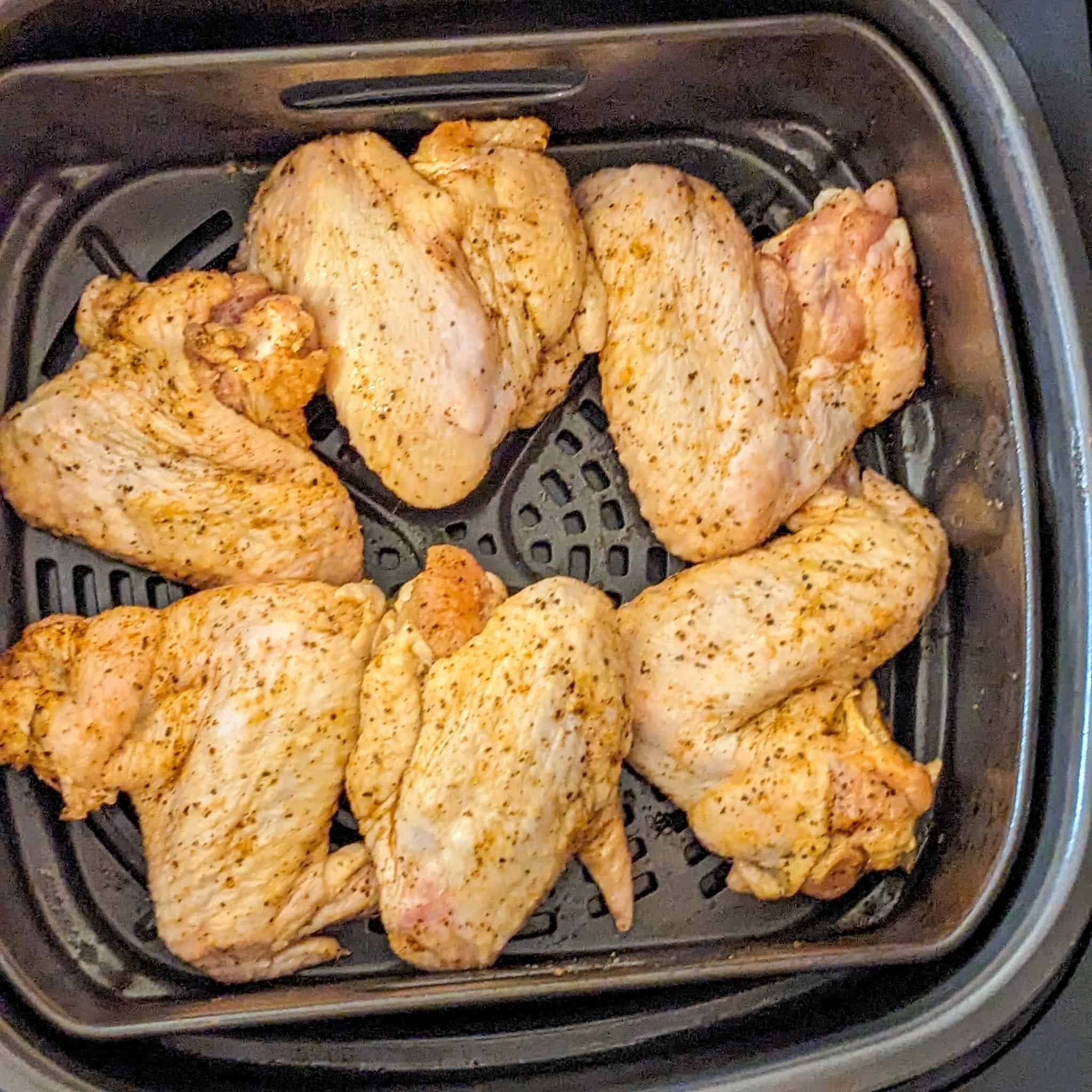 top view of raw whole chicken wings in an air fryer basket with the wing's tips tucked under neighboring wing for the Best Air Fryer Caribbean Style Citrus Chicken Wings recipe