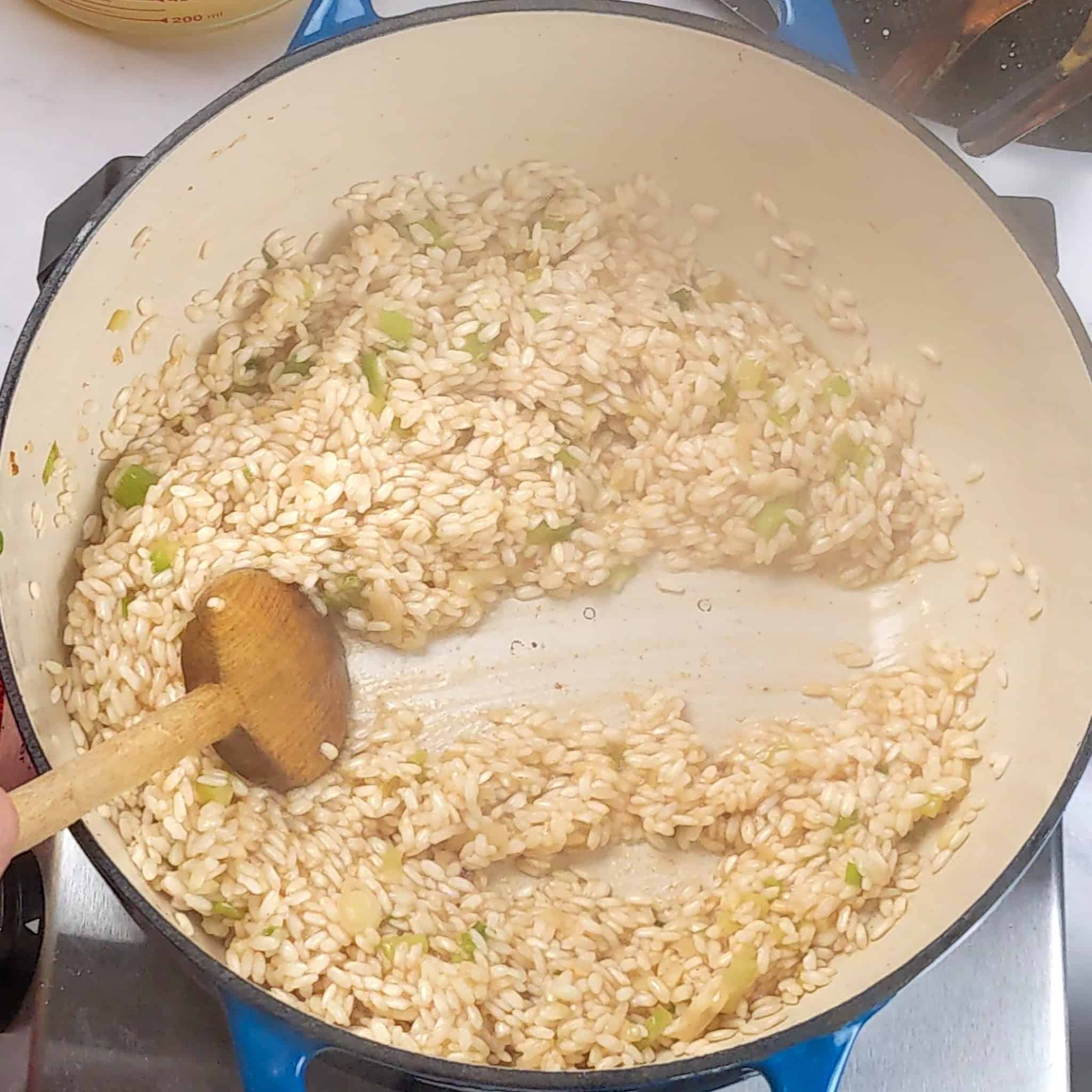 half way cooked risotto in a dutch oven with a wooden spoon split the risotto in the center