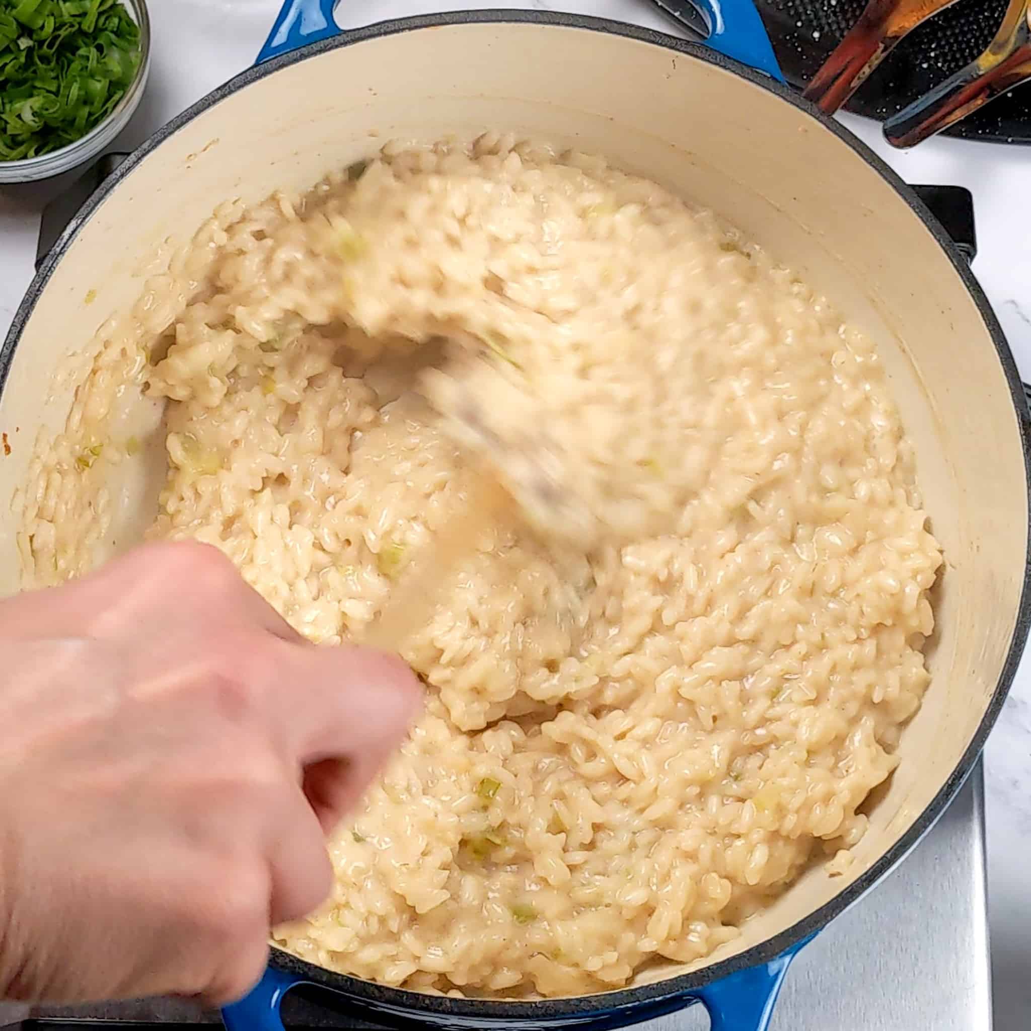creamy white cheddar cheese risotto being mixed with a wooden spoon