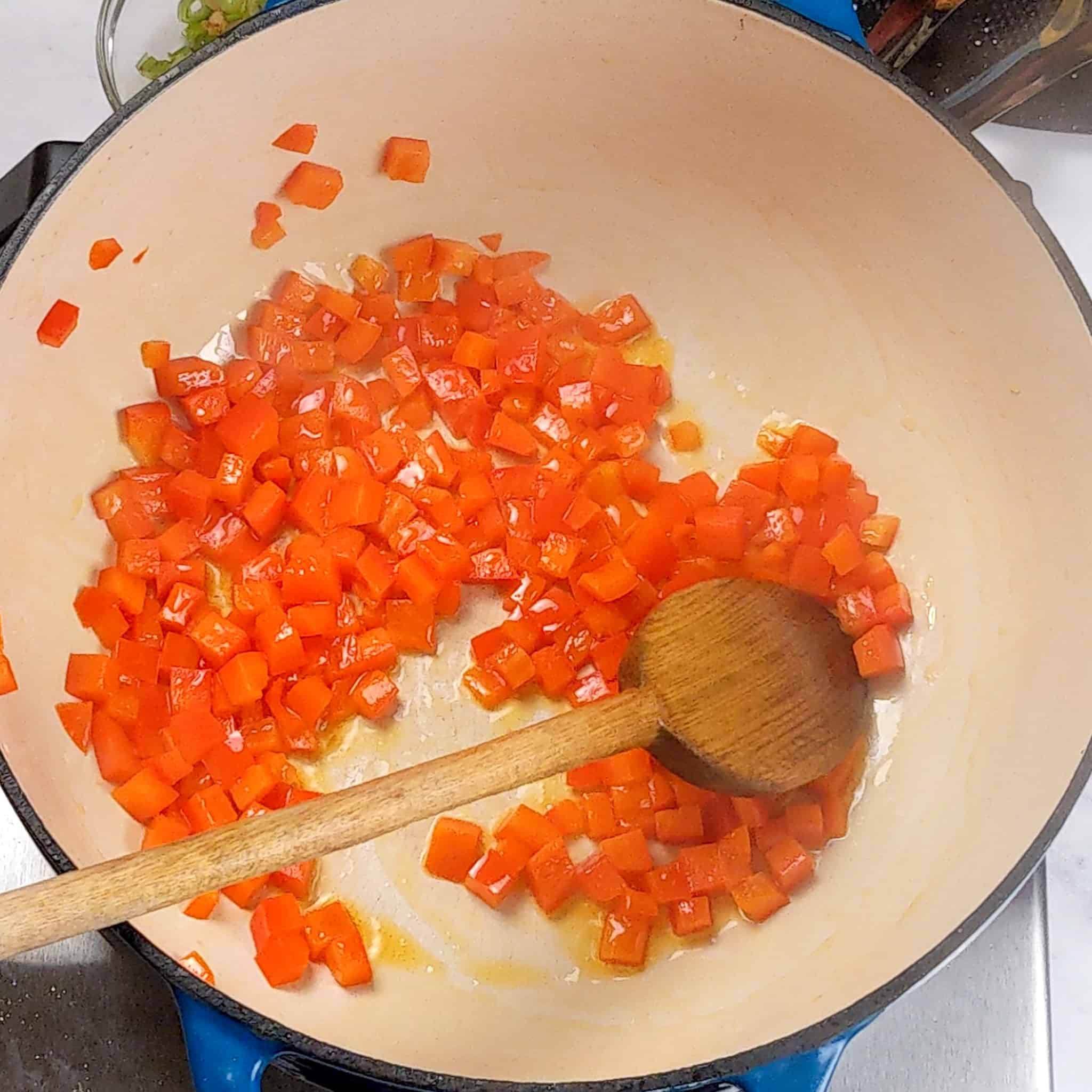 diced red bell pepper cooked in a dutch oven with a wooden spoon
