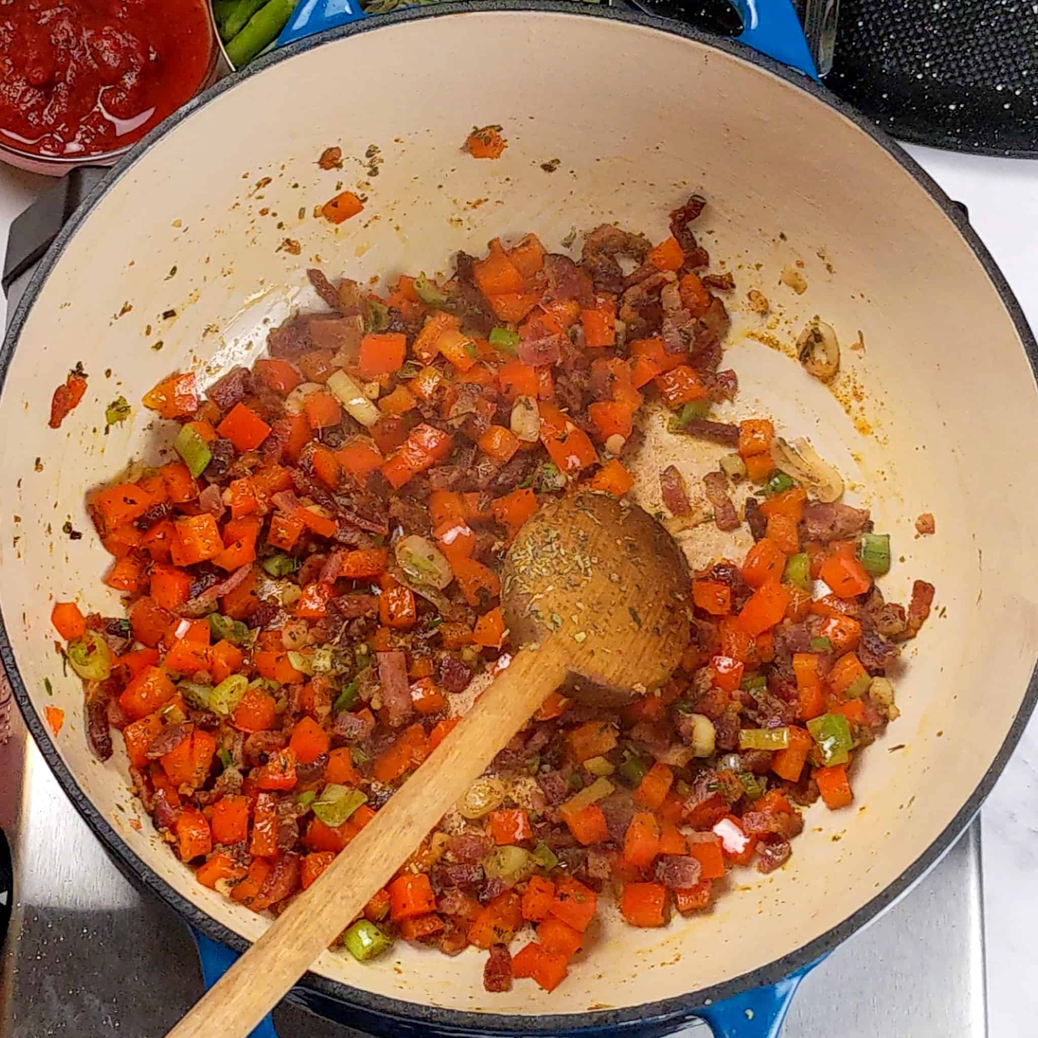 cooked diced red bell pepper with bacon, cooked sliced scallions and chopped garlic cooked in a pot with a wooden spoon