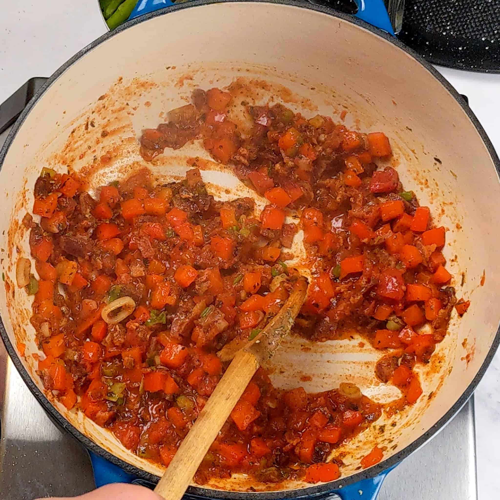 cooked diced red bell pepper with bacon, cooked sliced scallions, chopped garlic and tomato sauce cooked in a pot with a wooden spoon