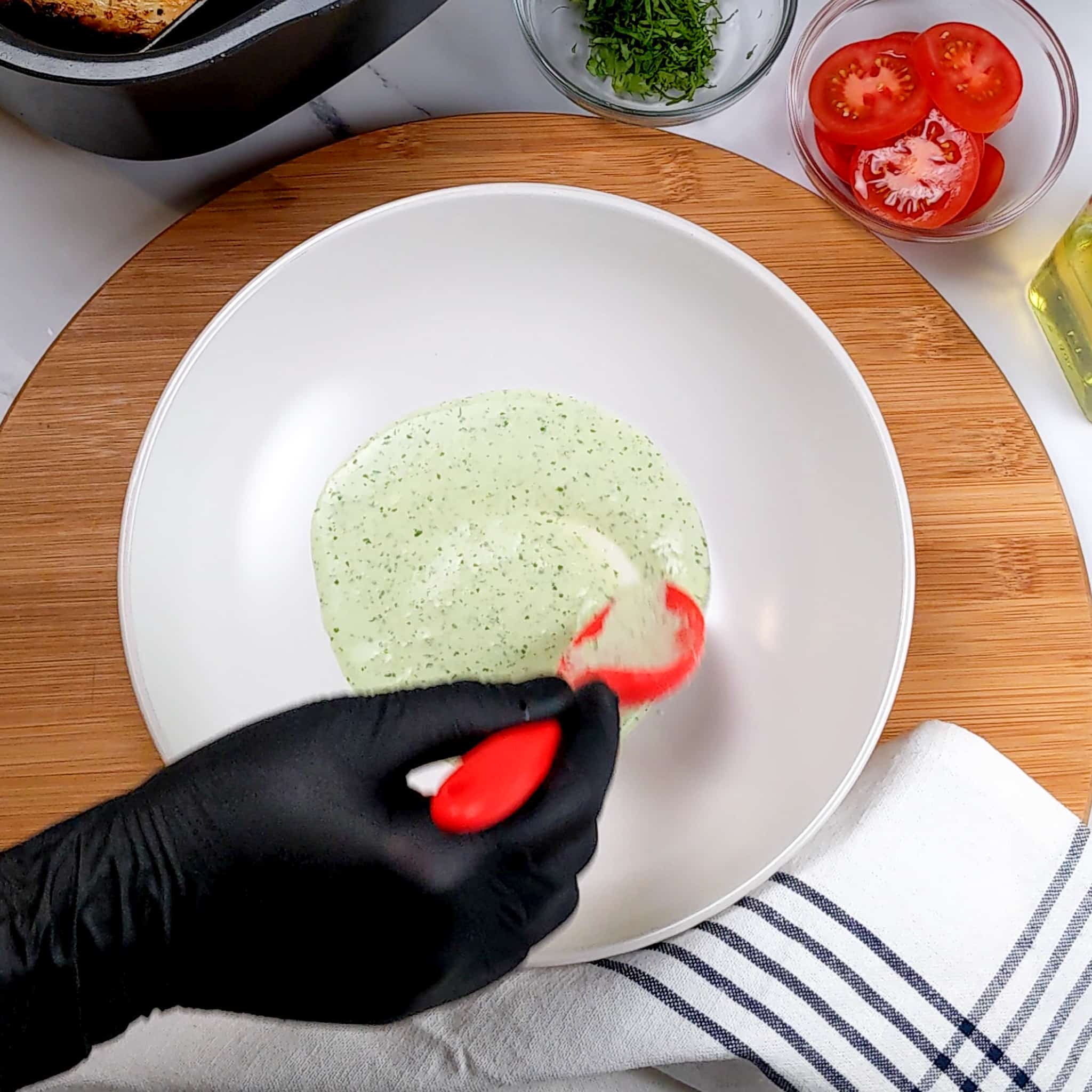 the spicy green jalapeno vinaigrette being plated in a wide rim bowl with a GIR silicone spoon by a gloved hand
