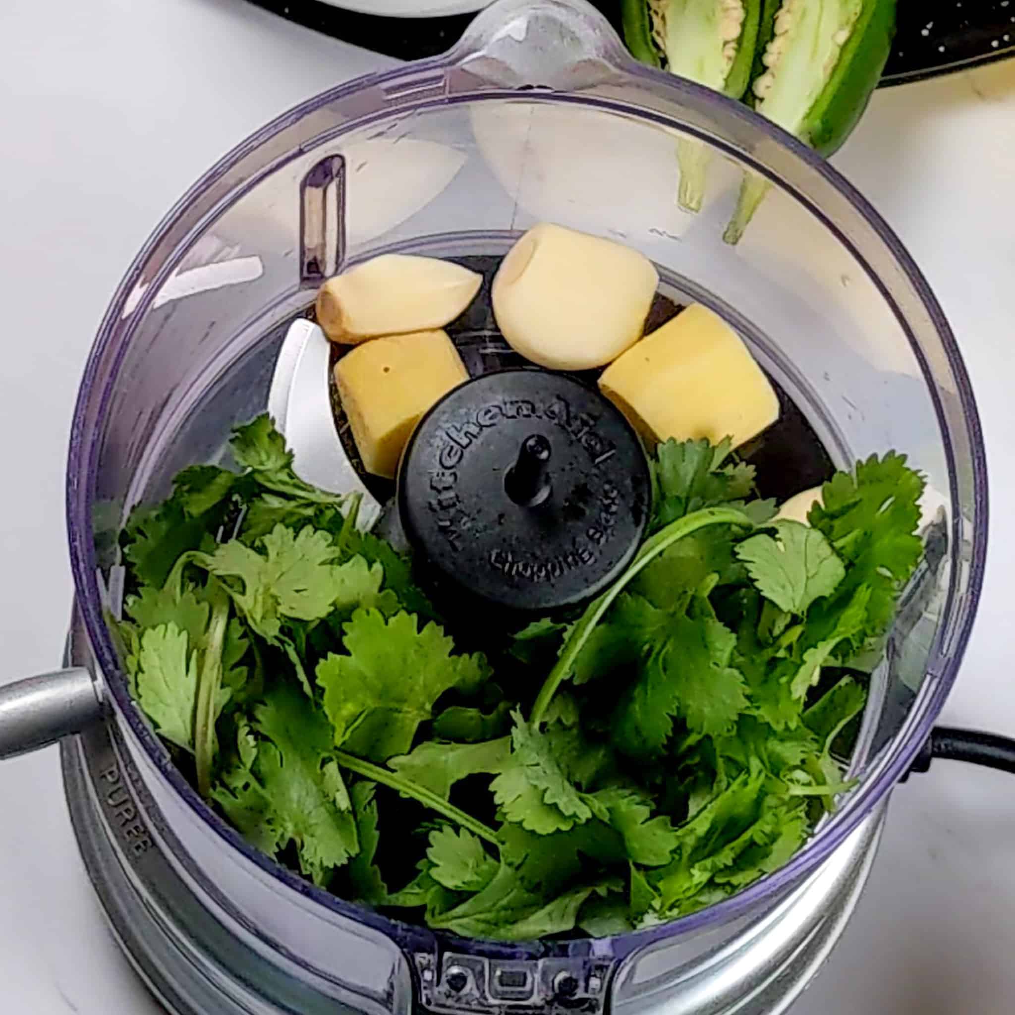 top view of food processor with fresh cilantro, garlic cloves and ginger chunks.