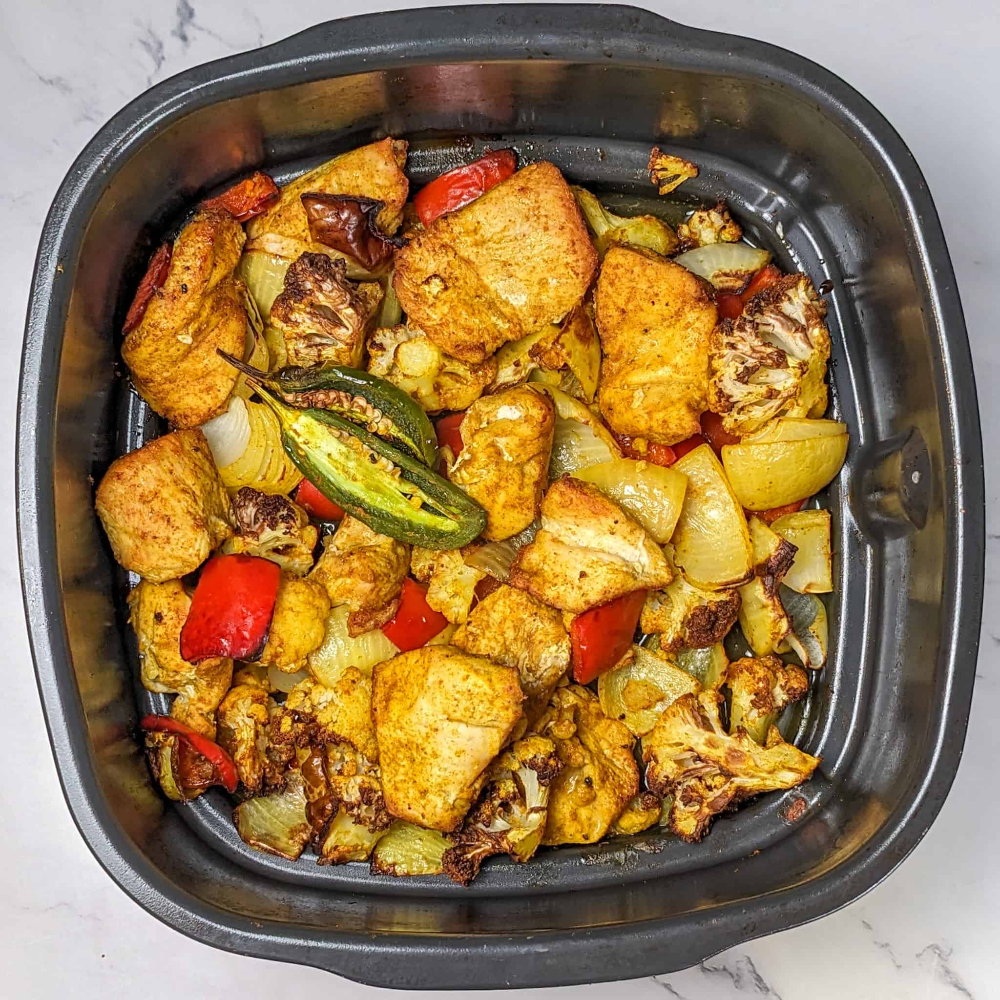 top view of the golden brown chicken and vegetables and jalapeno pepper for the Air Fryer Roasted Chicken Chickpeas Vegetable Curry recipe in the Ninja Foodi 5-in-1 Indoor Electric Grill roasting pan.
