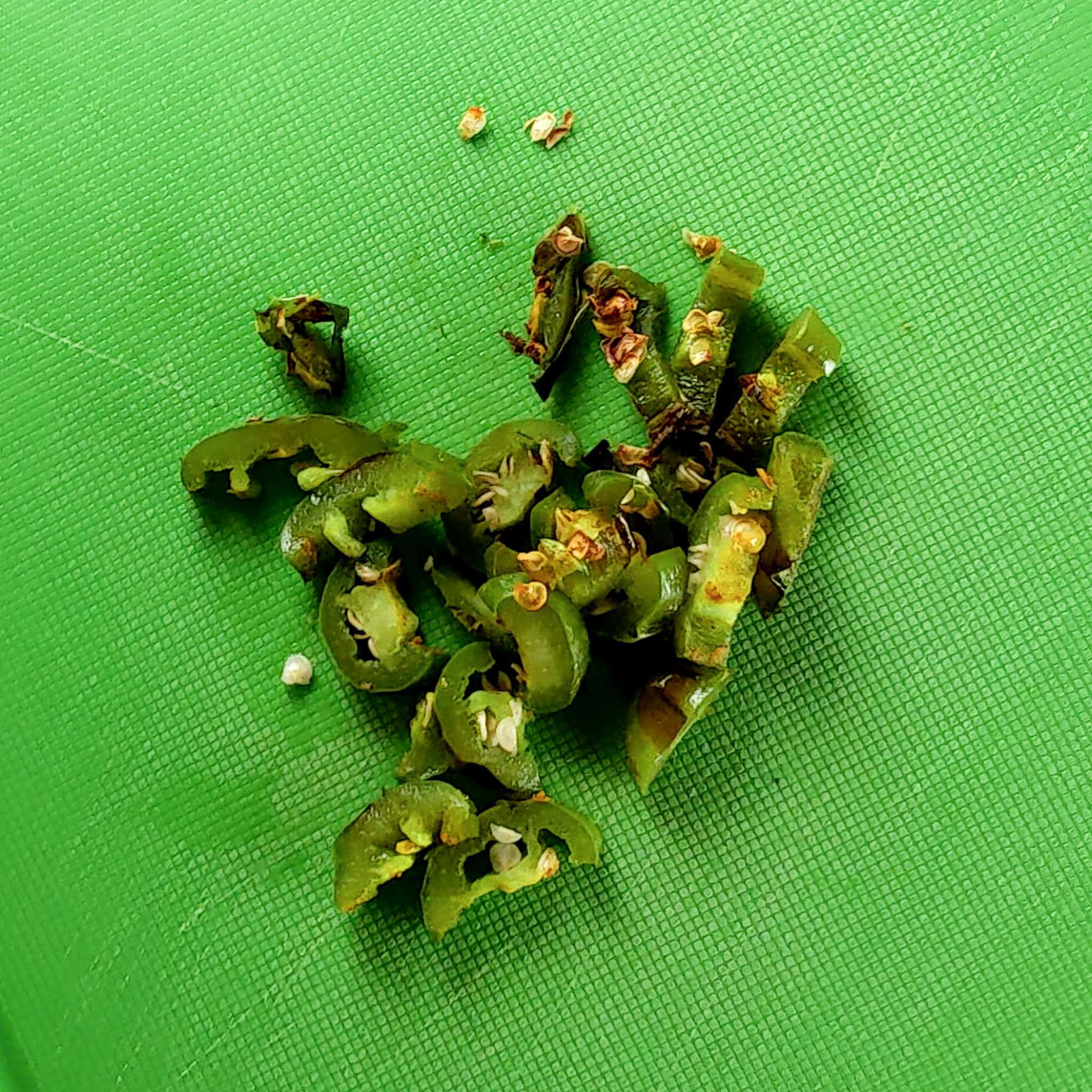 half moon sliced roasted air-fried jalapeno with seeds on a plastic cutting board.