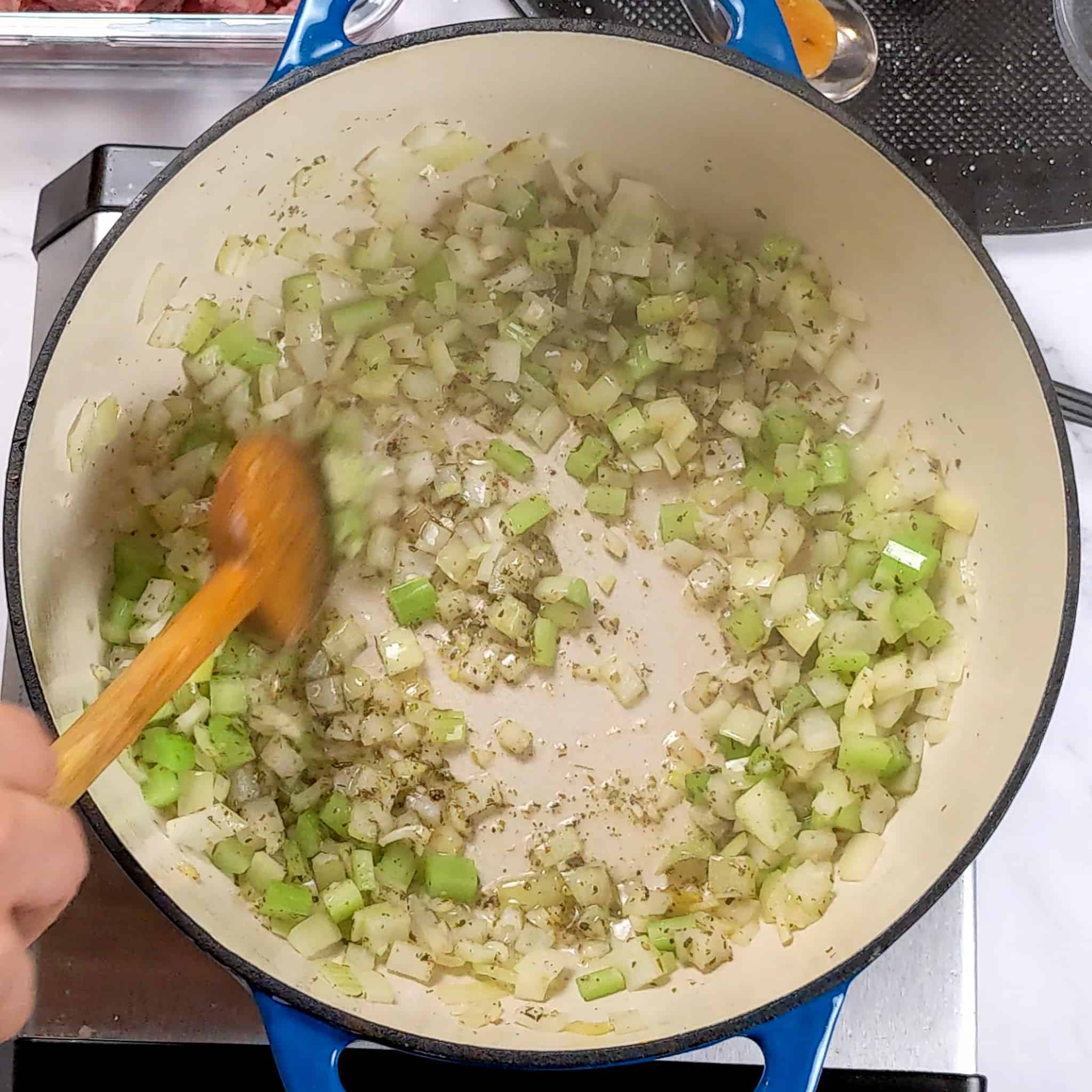 diced onion and celery, chopped garlic with dried thyme cooking in a a enameled dutch oven being stirred with a wooden spoon