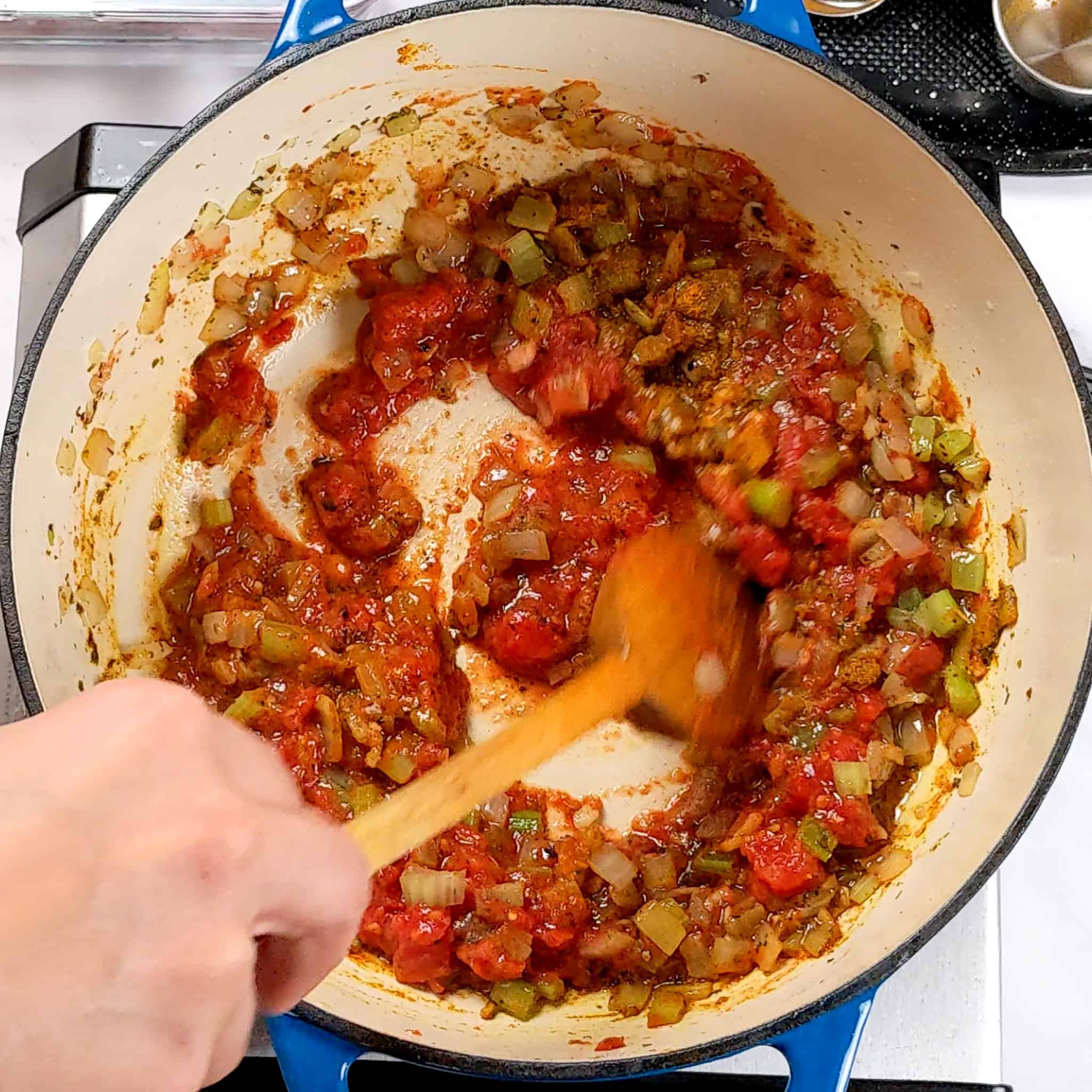 a thick tomato sauce in paste consistency mixed with the onion, celery mixture being stirred with a wooden spoon