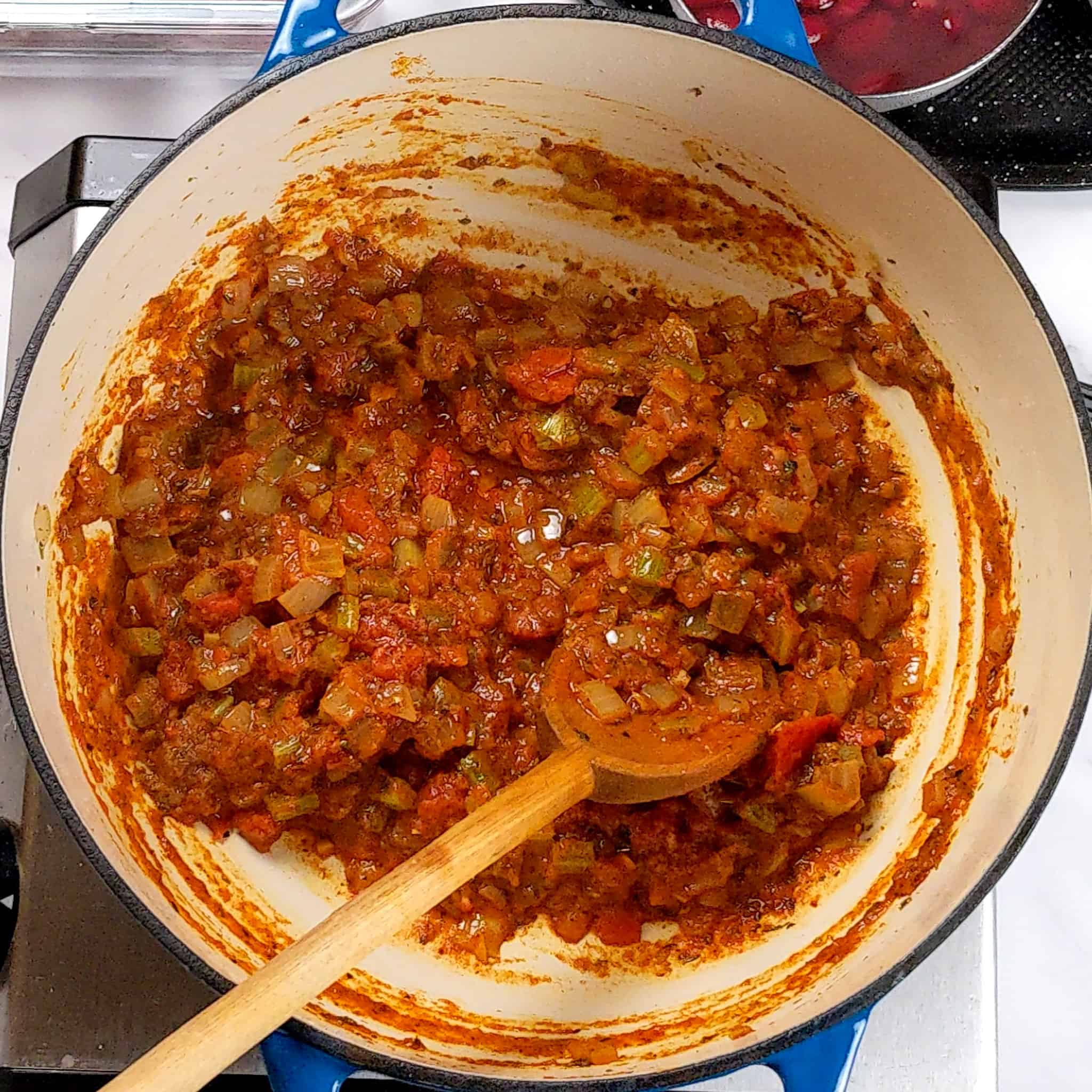 a thick tomato sauce in paste consistency mixed with the onion, celery mixture being stirred with a wooden spoon that has been cooked down with less liquid
