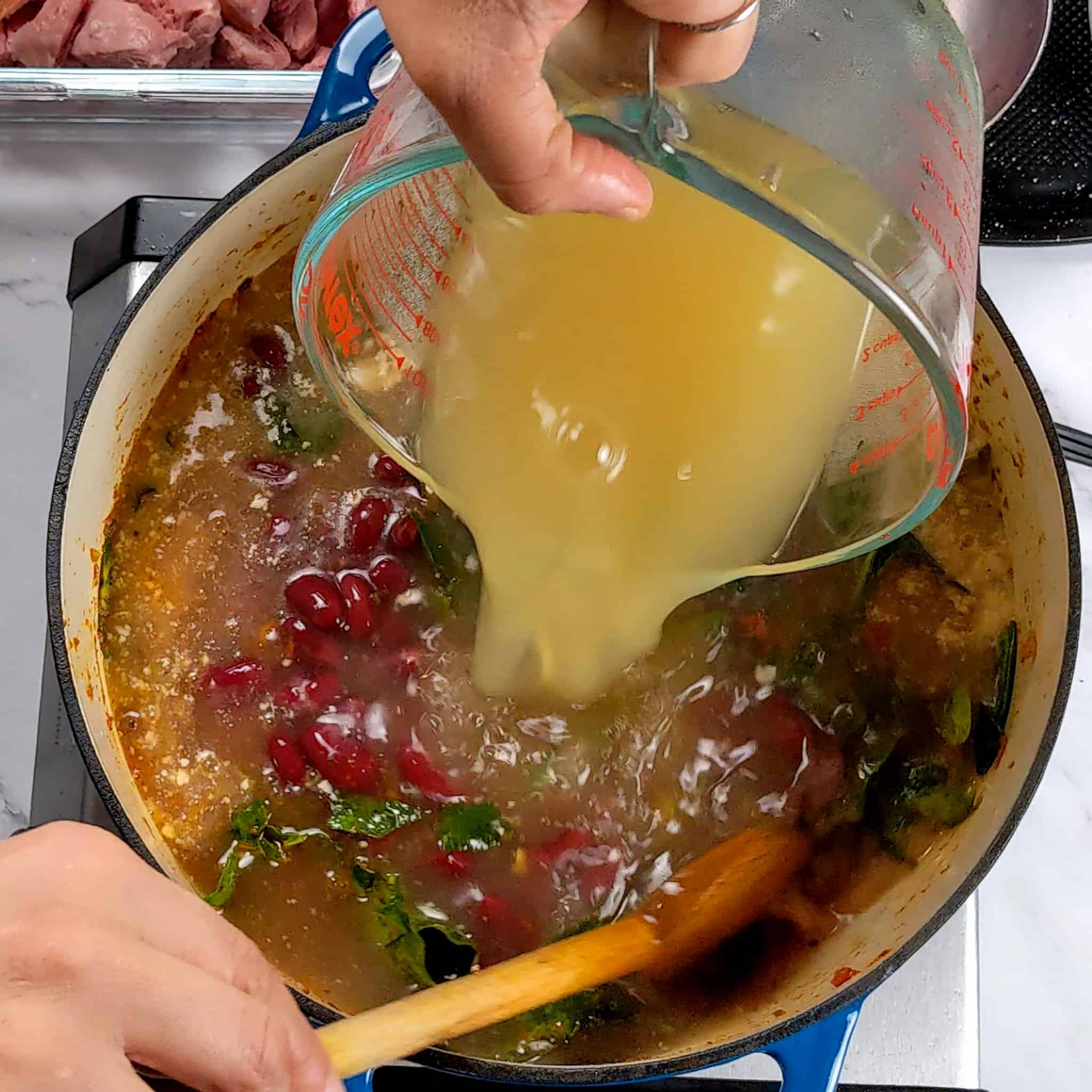 chicken stock in a pyrex glass measuring cup being poured into the soup base