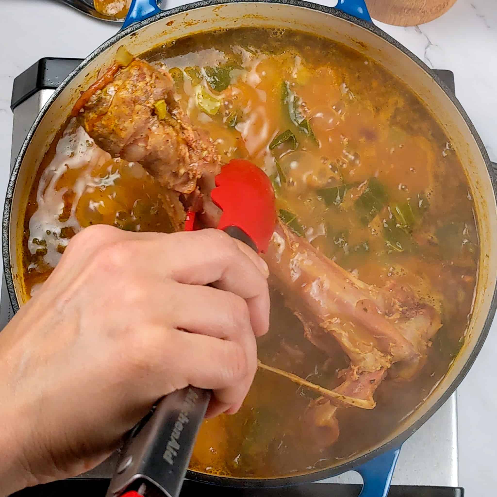 a kitchenaid silicone spatula pulling out the turkey leg bone from the soup