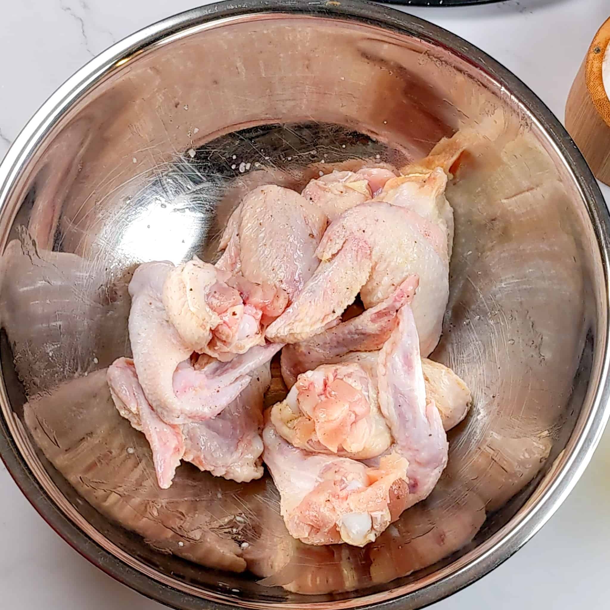 raw salt, pepper and oil seasoned whole chicken wings in a large stainless steel mixing bowl