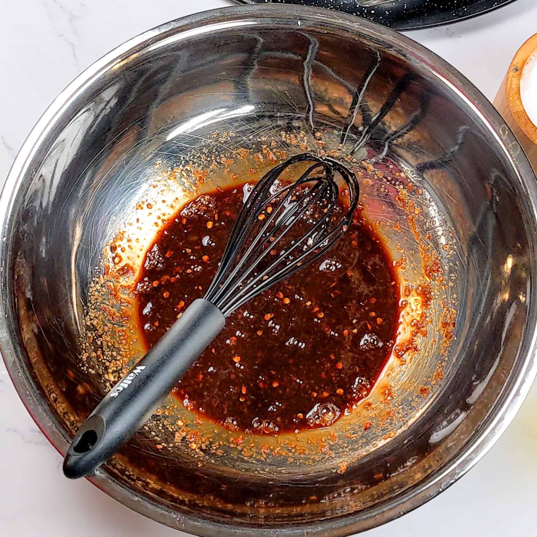 large stainless steel mixing bowl with the sticky date teriyaki sauce with a silicone whisk resting in the bowl