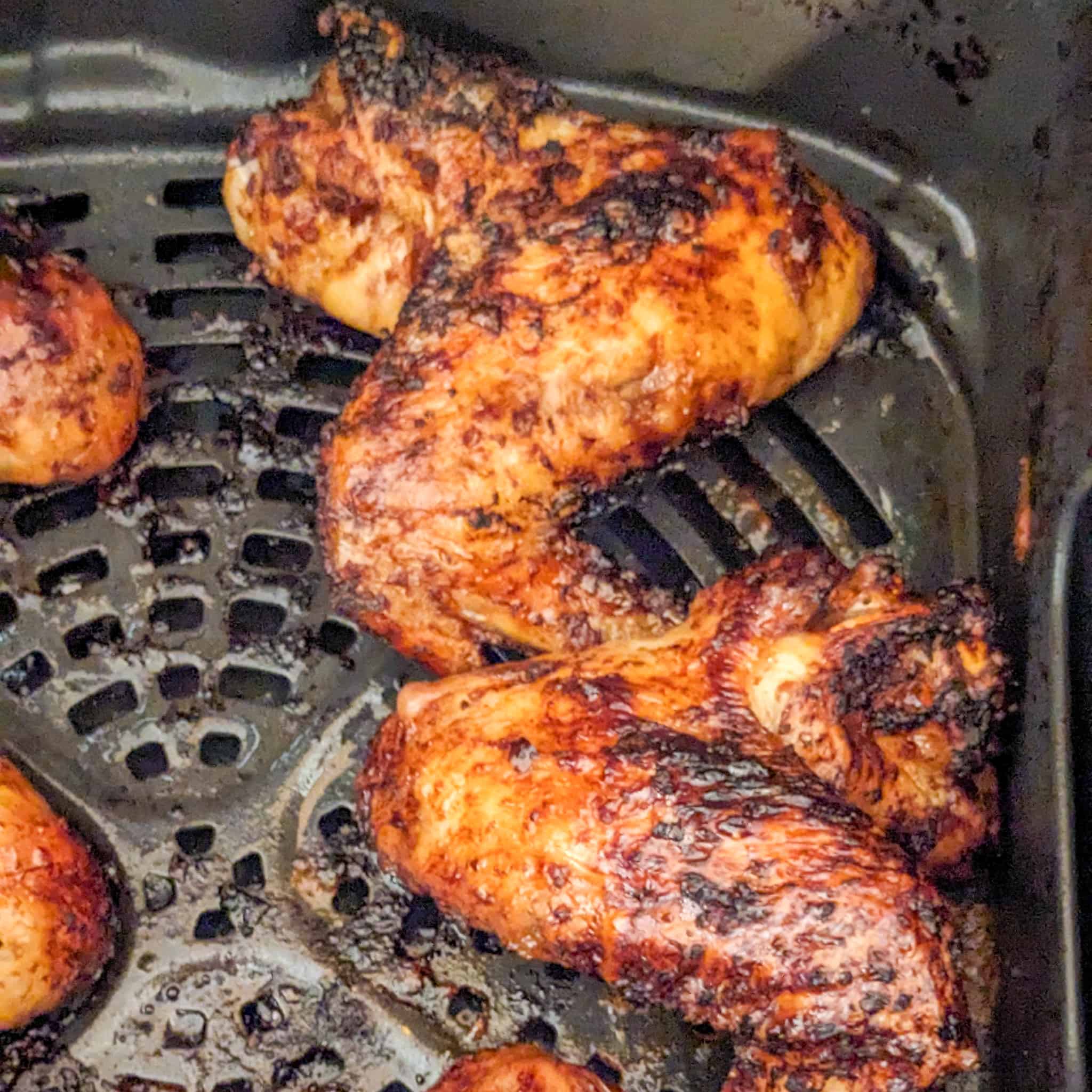 whole chicken wings with tips tucked under the neighboring chicken wing in an air fryer basket cooked in the air fryer after being basted with the sticky date teriyaki sauce