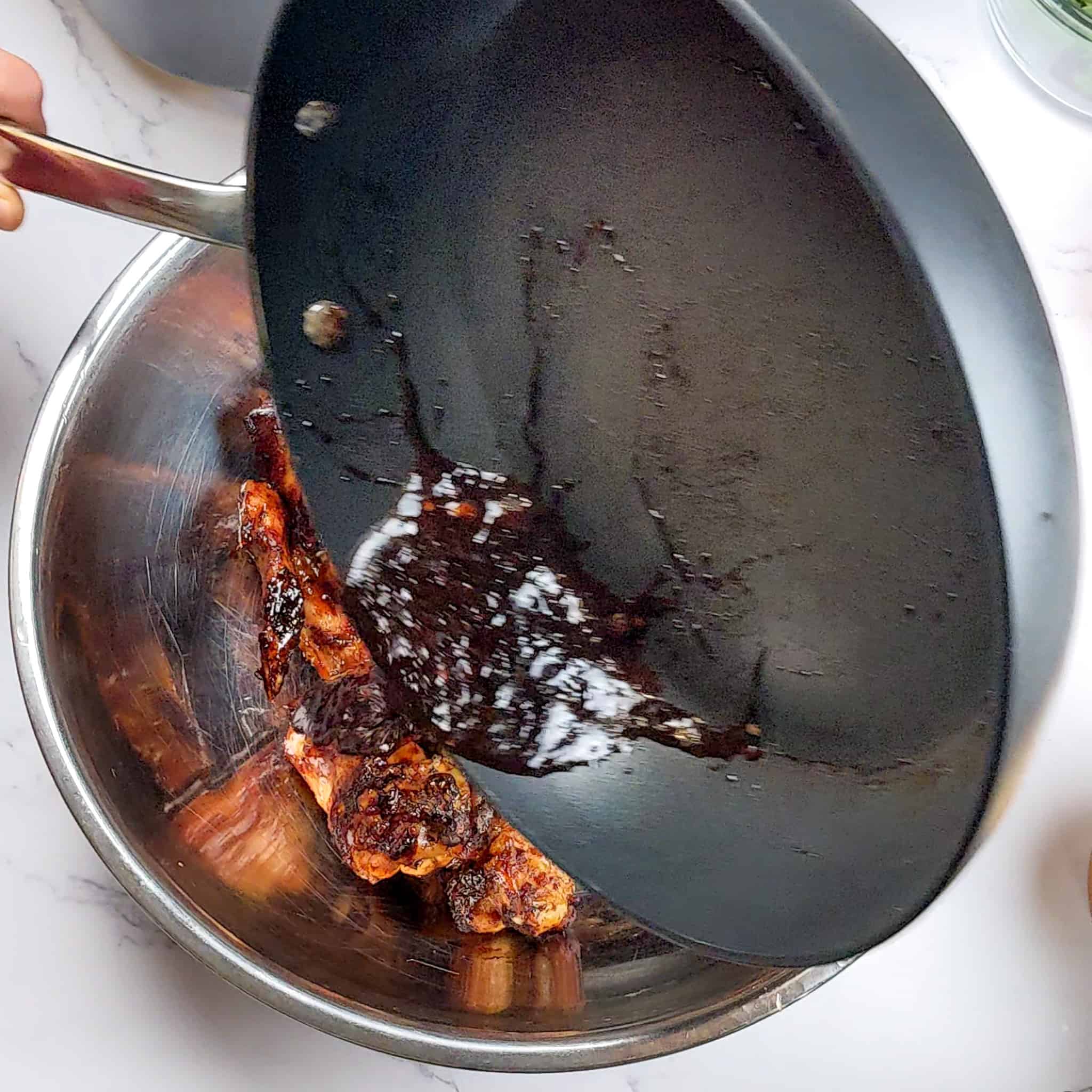 the sticky date teriyaki sauce being poured over the cooked whole chicken wings in a large mixing bowl