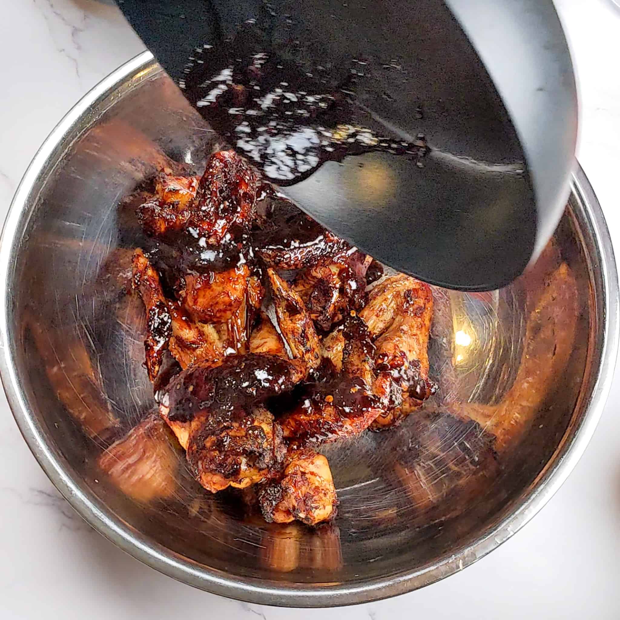 the sticky date teriyaki sauce being poured over the cooked whole chicken wings in a large mixing bowl