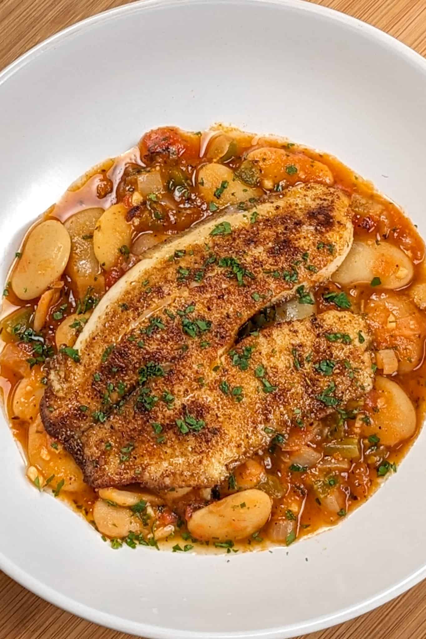 Top view of Pan-Seared Cajun Spiced Tilapia on White Bean Stew recipe in a wide rim bowl.