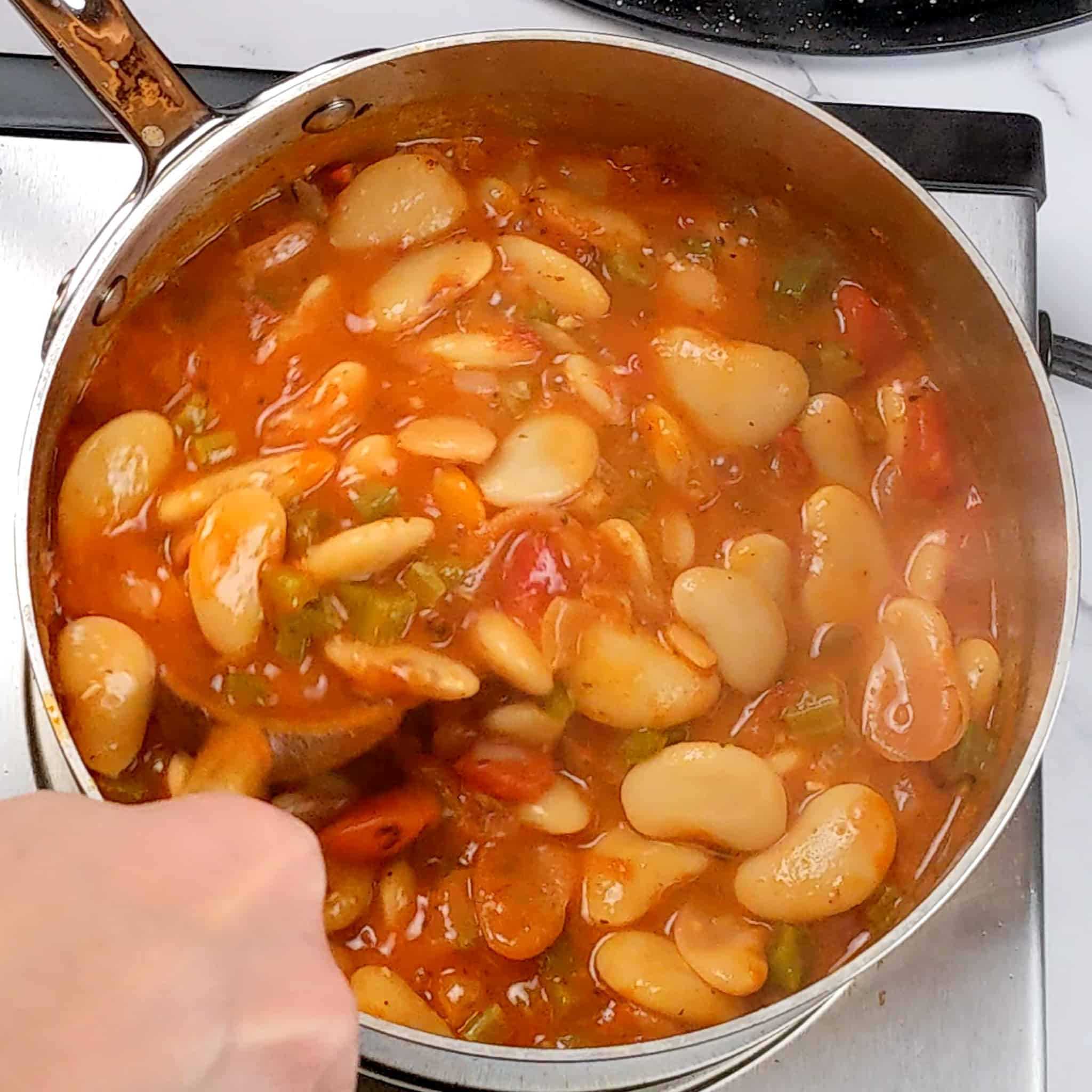 tomato sauce simmering with butter beans in a sauce pan being stirred with a wooden spoon
