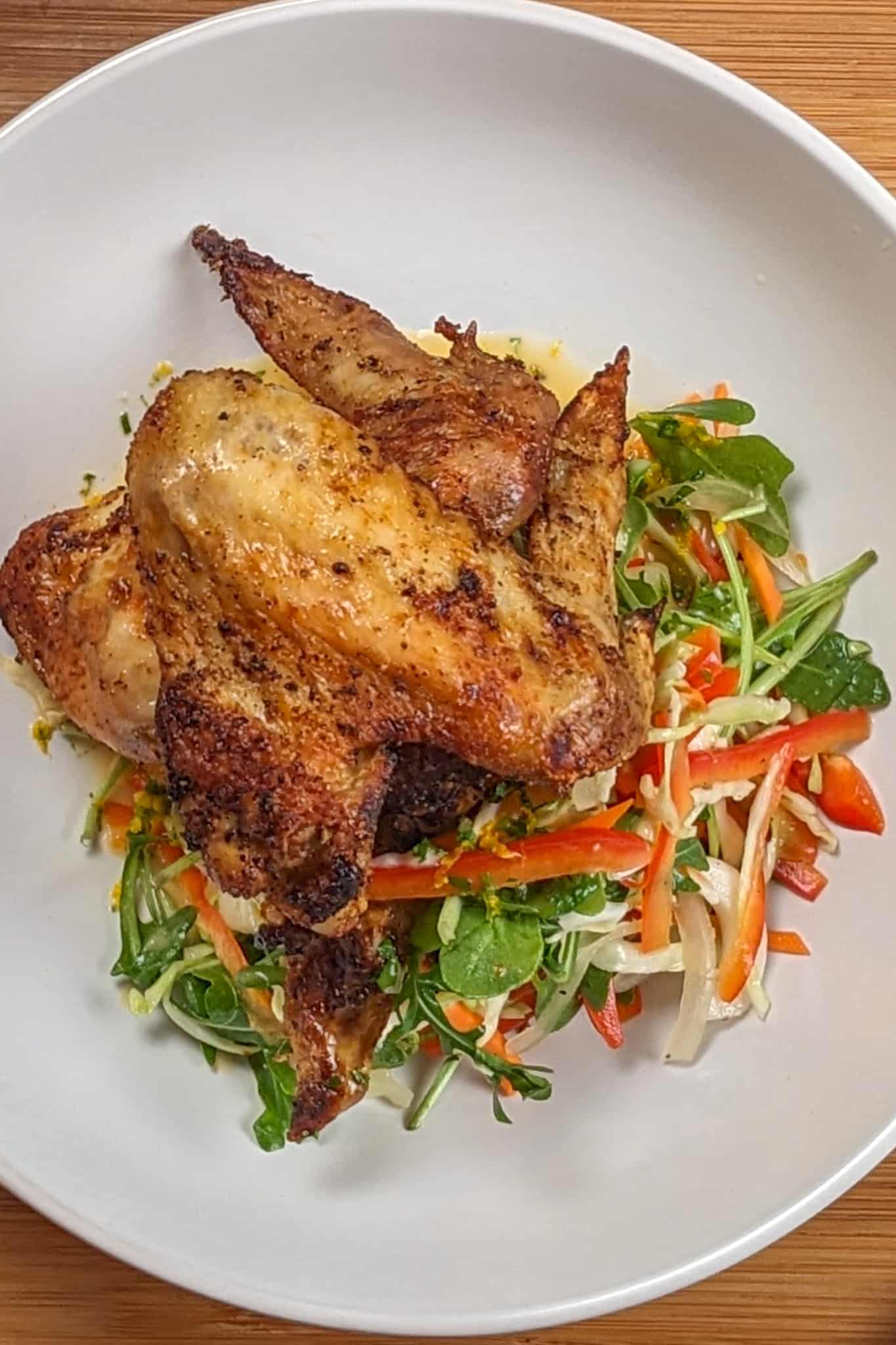 top view of the Best Air Fryer Caribbean Style Citrus Chicken Wings next to a salad with vinaigrette in a wide rim bowl