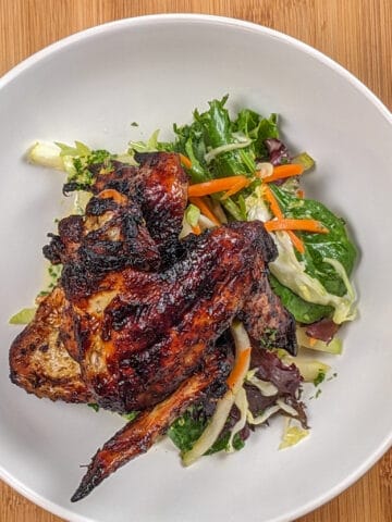 top view the Crispy Air Fryer Honey Jerk Rubbed Chicken Wings recipe next to marinated vegetables with greens and vinaigrette in a wide rim bowl