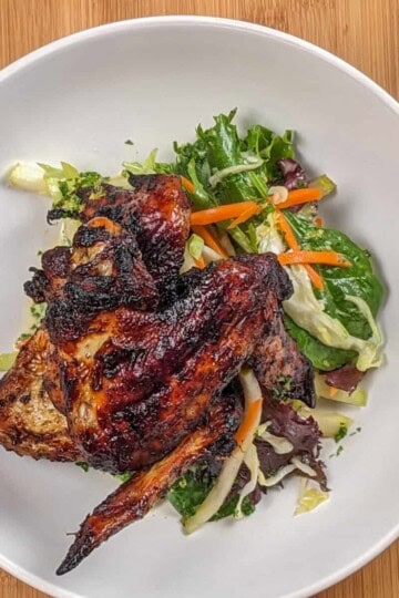 top view the Crispy Air Fryer Honey Jerk Rubbed Chicken Wings recipe next to marinated vegetables with greens and vinaigrette in a wide rim bowl