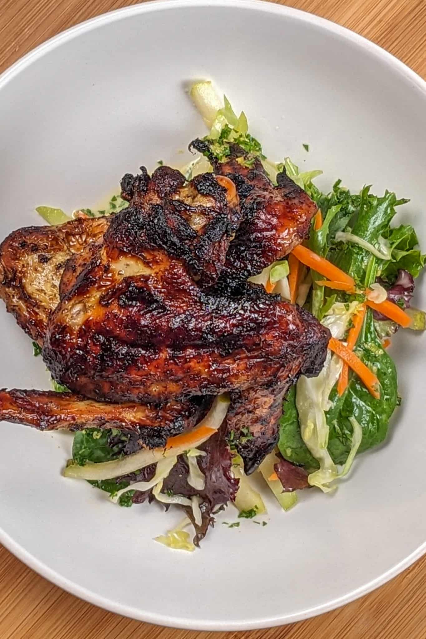 top view of the Crispy Air Fryer Honey Jerk Rubbed Chicken Wings recipe next to marinated vegetables with greens and vinaigrette in a wide rim bowl