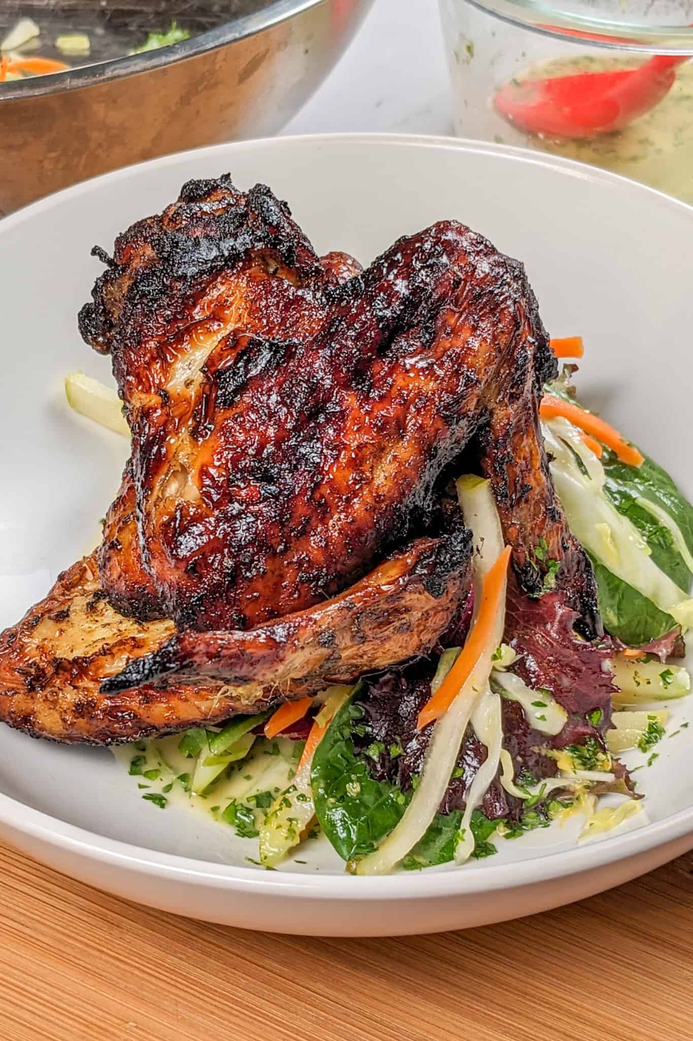 Side view of the Crispy Air Fryer Honey Jerk Rubbed Chicken Wings recipe next to marinated vegetables with greens and vinaigrette in a wide rim bowl