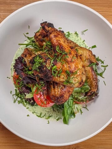 top view Plated Quick Air Fryer Lime Chicken Wings on greens with sliced campari tomatoes with Spicy Green Sauce on the bottom and the whole dish garnished with chiffonade herbs in a wide rim bowl