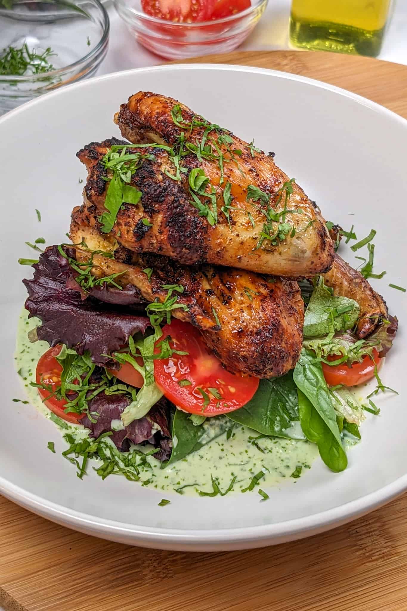 side view Plated Quick Air Fryer Lime Chicken Wings on greens with sliced campari tomatoes with Spicy Green Sauce on the bottom and the whole dish garnished with chiffonade herbs in a wide rim bowl