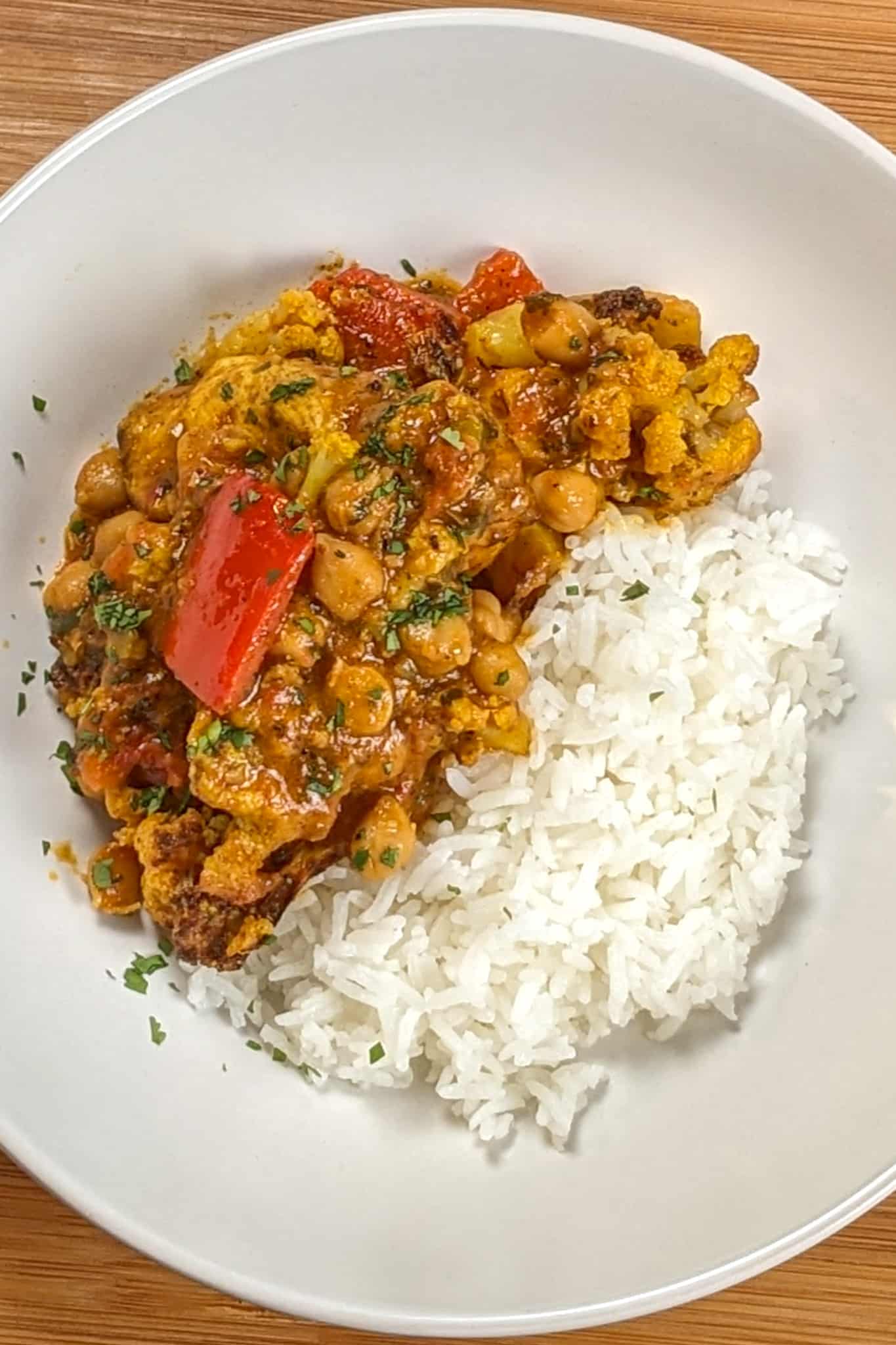 top view of the Air Fryer Roasted Chicken Chickpeas Vegetable Curry recipe in a wide rim bowl with a side of basmati rice.