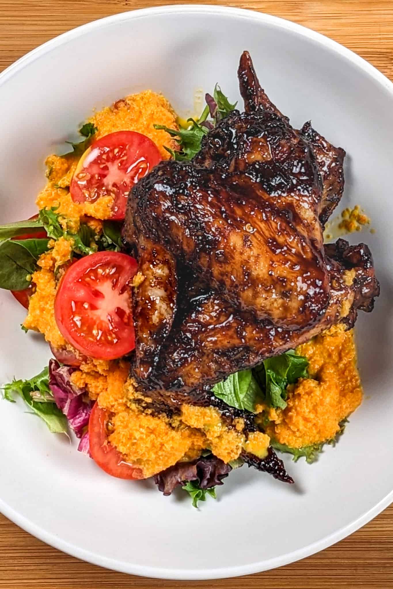 top view of the Easy Air Fryer Sticky Date Teriyaki Chicken Wings next to a salad of mixed greens sliced campari tomatoes with carrot ginger dressing in a wide rim bowl