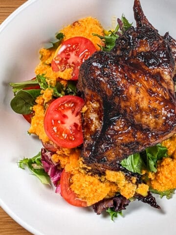 top view of the Easy Air Fryer Sticky Date Teriyaki Chicken Wings next to a salad of mixed greens sliced campari tomatoes with carrot ginger dressing in a wide rim bowl