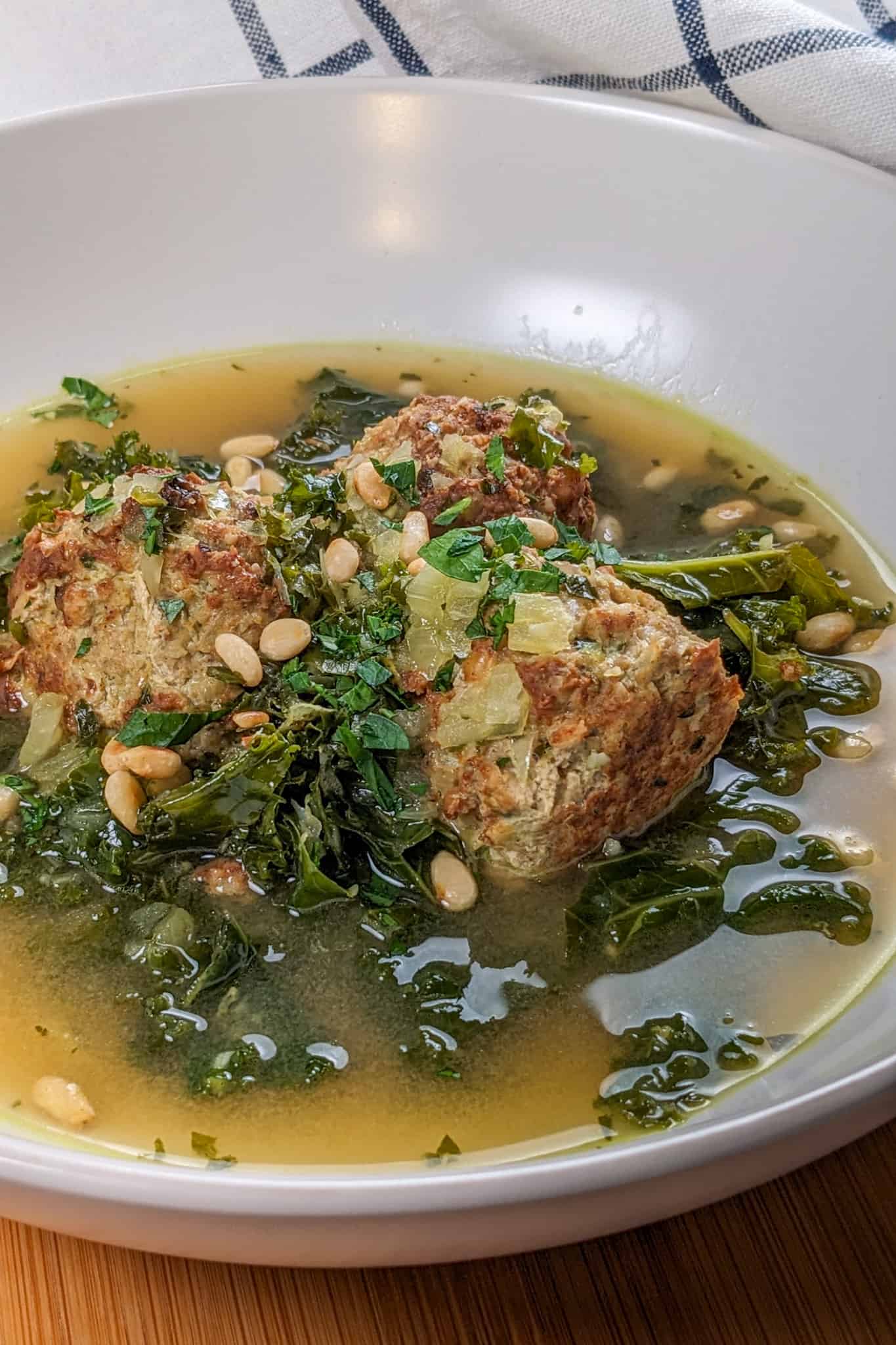 Side view of the Easy and Healthy Spicy Turkey Meatball Kale Soup om a wide rim bowl garnished with toasted pine nuts