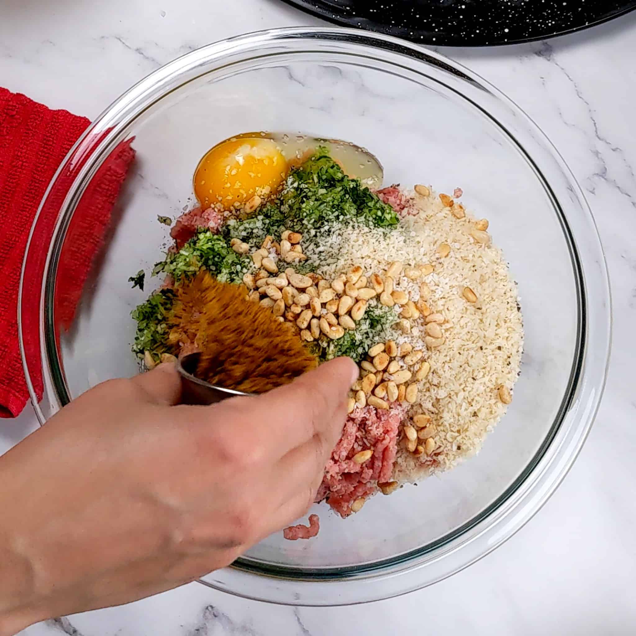 clear glass pyrex mixing bowl with the meatball ingredients being sprinkled with shawarma spice blend