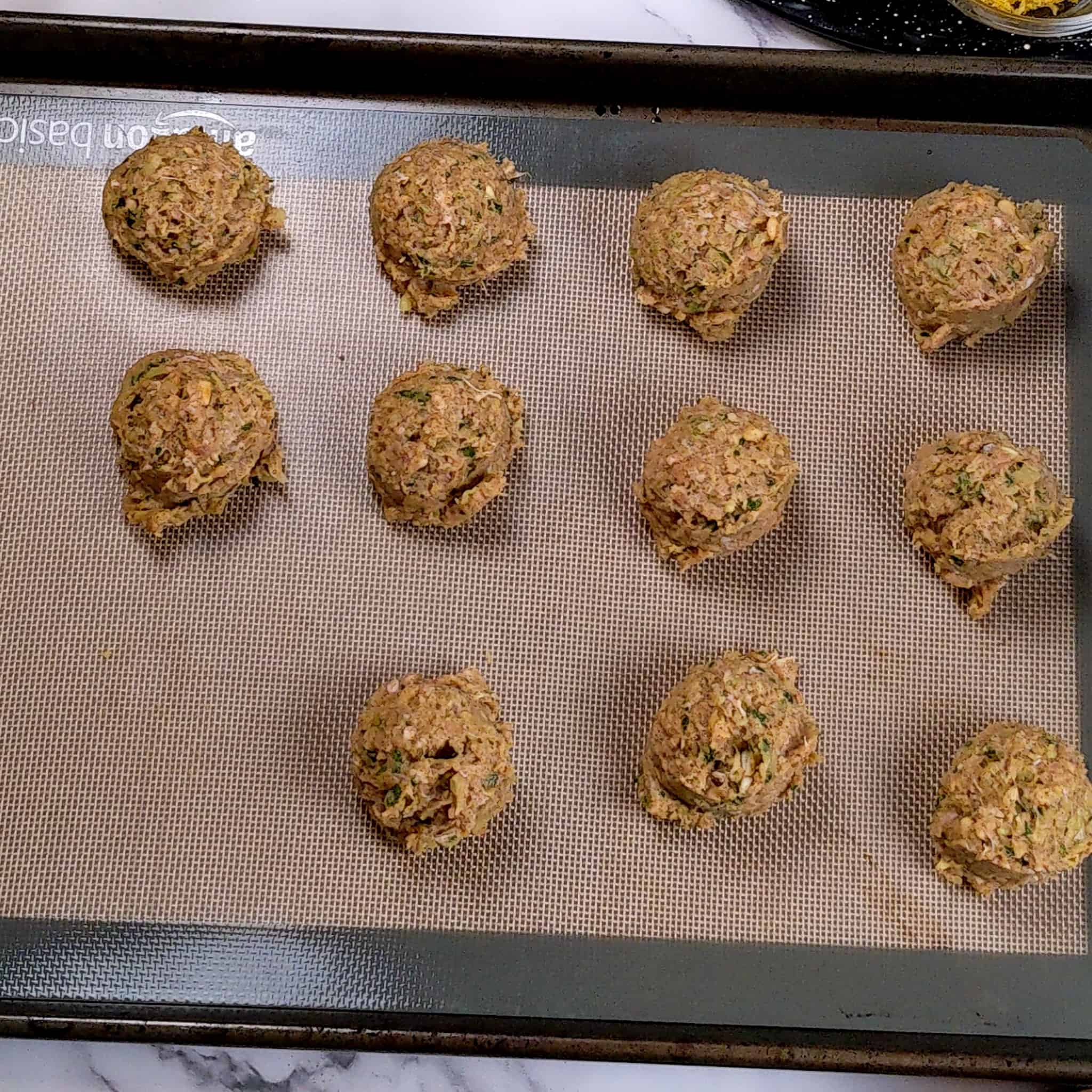 evenly scooped meatballs on a silicone sheet layered sheet pan
