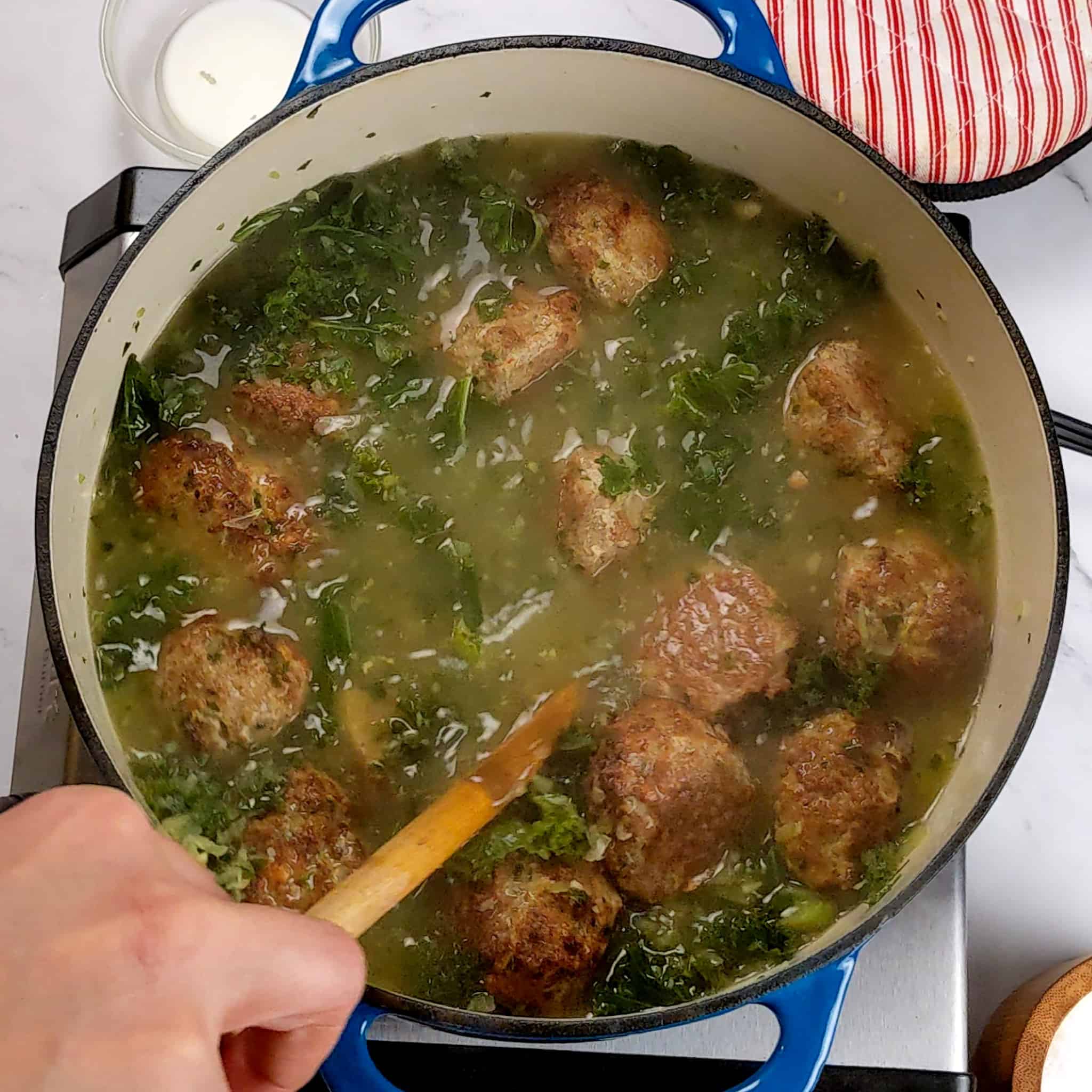 meatballs in a kale broth being stirred with a wooden spoon for the Easy and Healthy Spicy Turkey Meatball Kale Soup