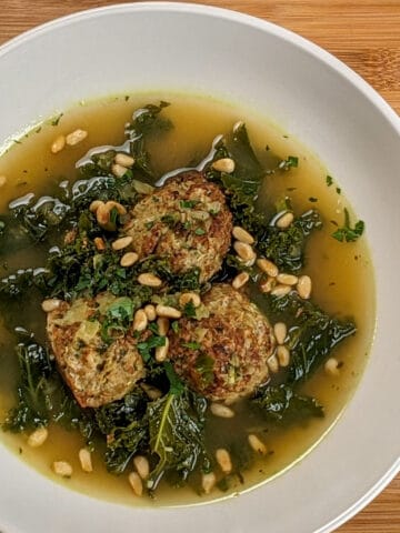 top close up view of the Easy and Healthy Spicy Turkey Meatball Kale Soup in a wide rim bowl garnished with toasted pinenuts