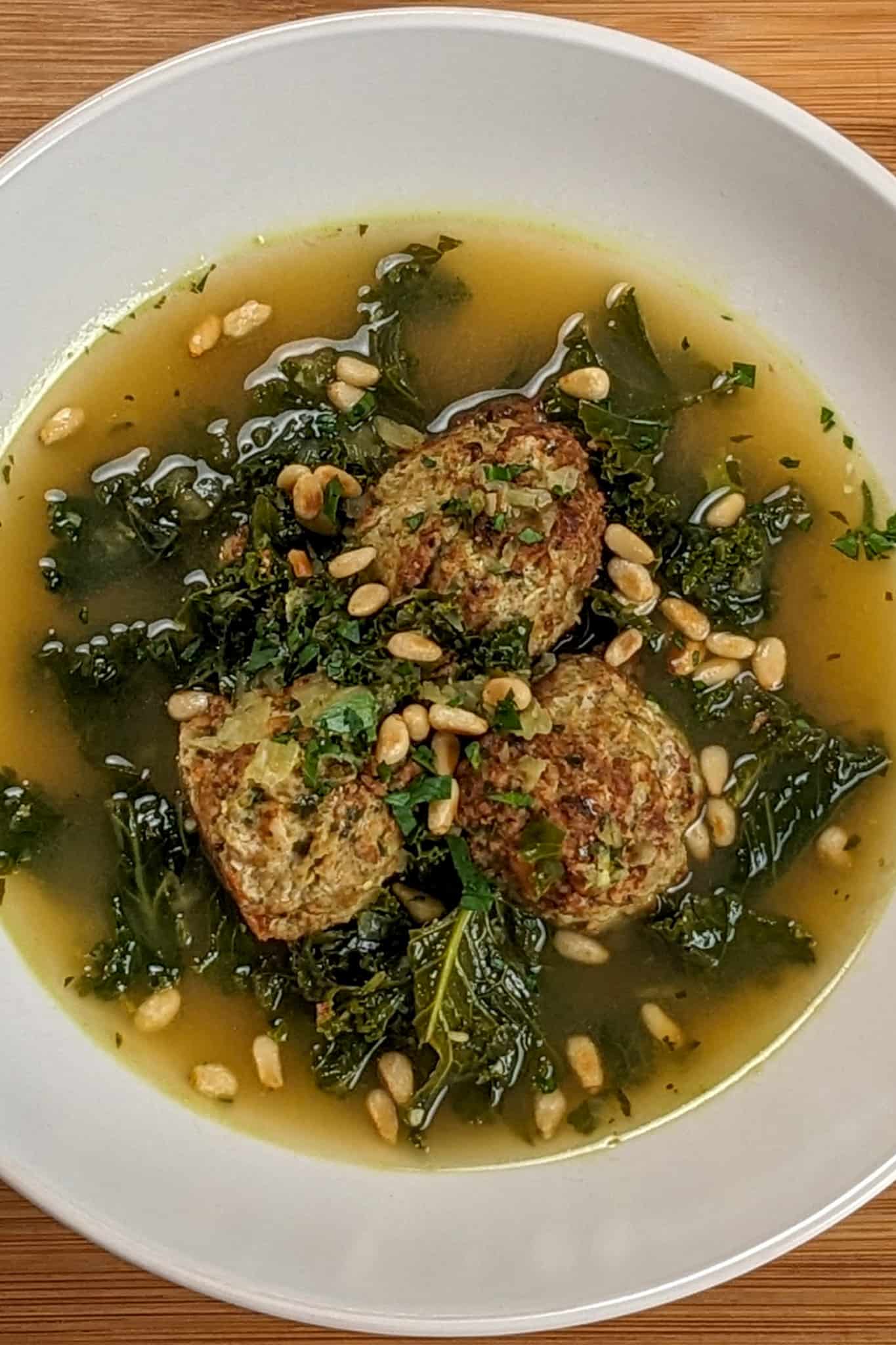 top close up view of the Easy and Healthy Spicy Turkey Meatball Kale Soup in a wide rim bowl garnished with toasted pine nuts