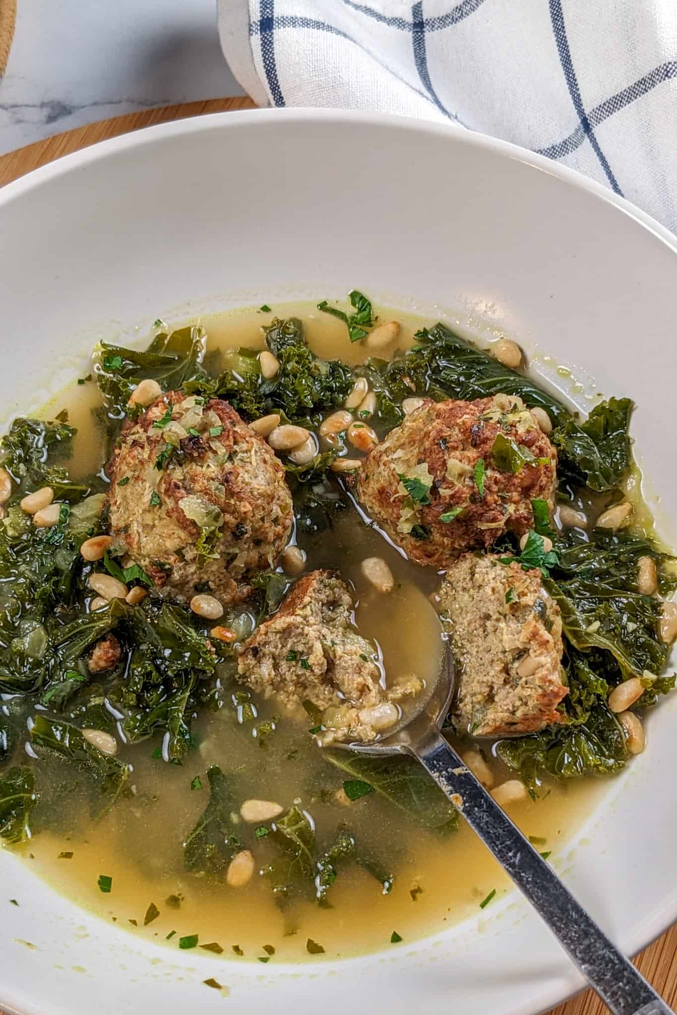 top view of the turkey meatball kale soup with one of the meatballs divided with a stainless steel korean spoon in a wide rim soup bowl.