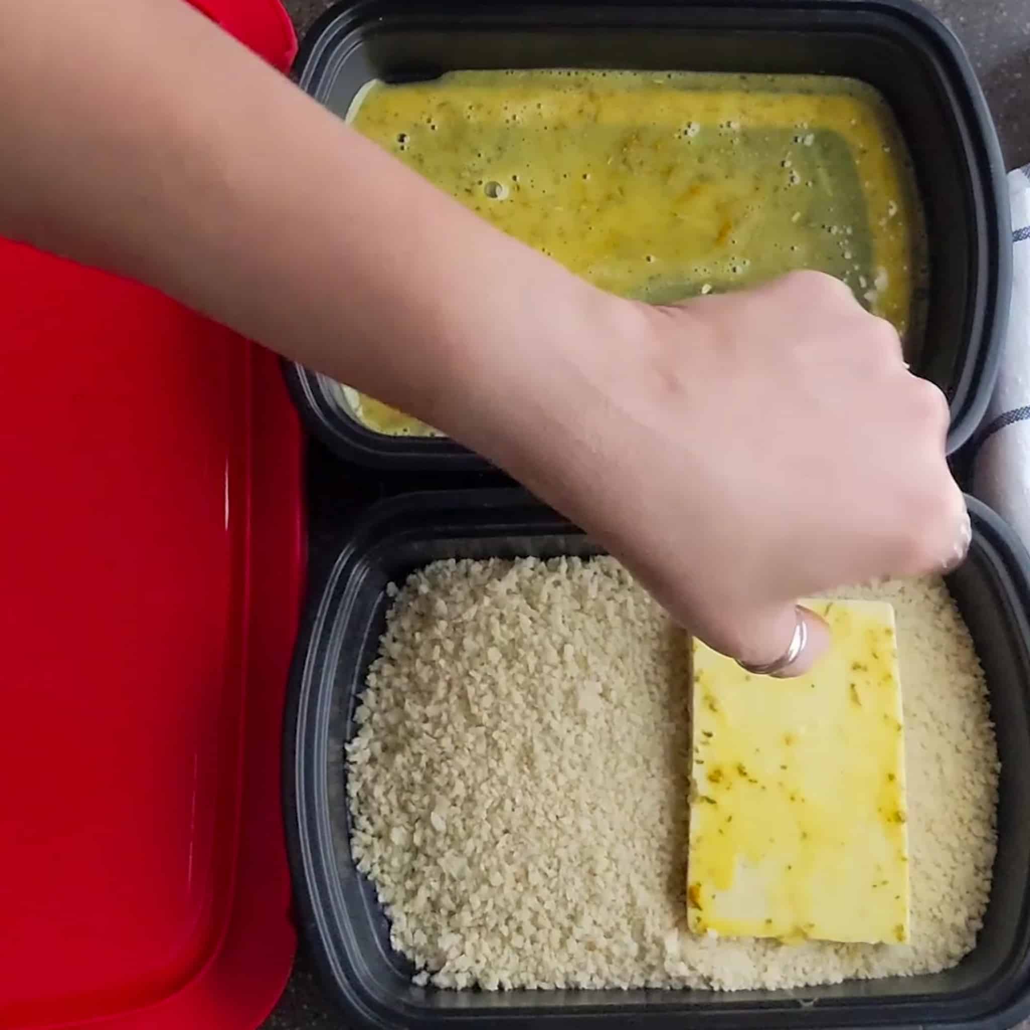 egg dipped large sliced tofu covered in japanese panko in a shallow container filled with more panko.