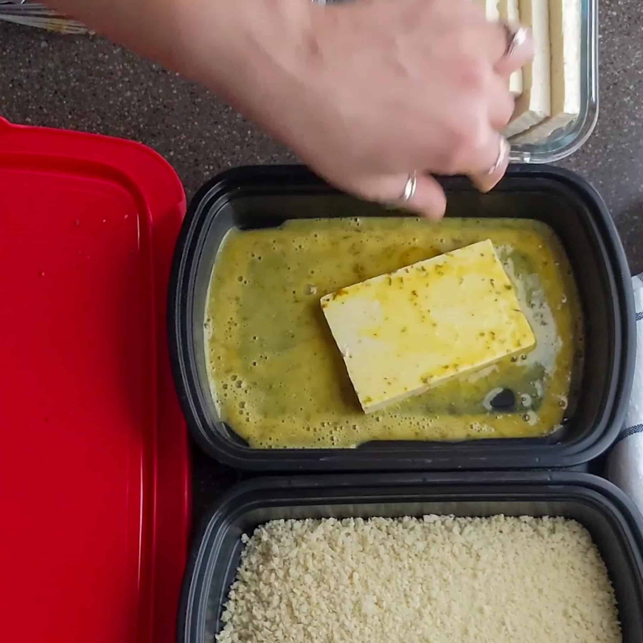 large sliced todu laying in an egg wash in a shallow container