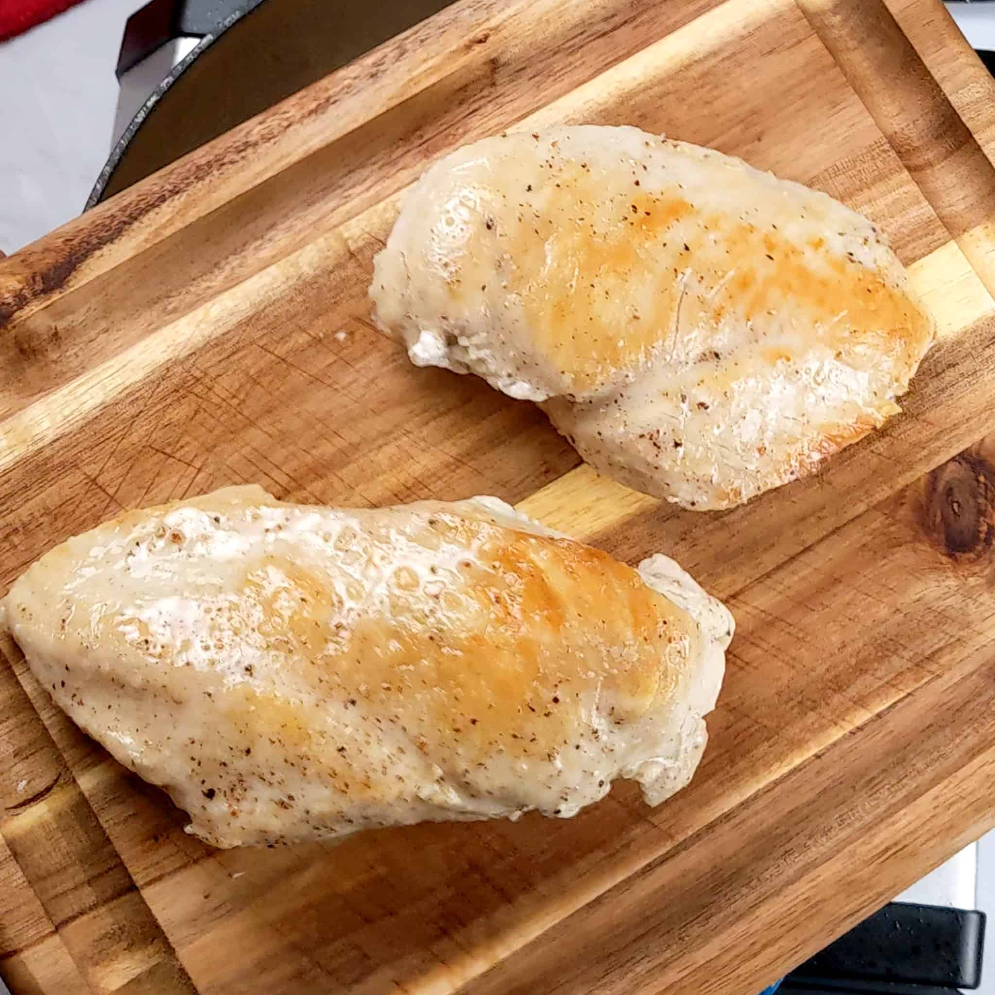 two cooked seared chicken breast resting on a small wooden cutting board
