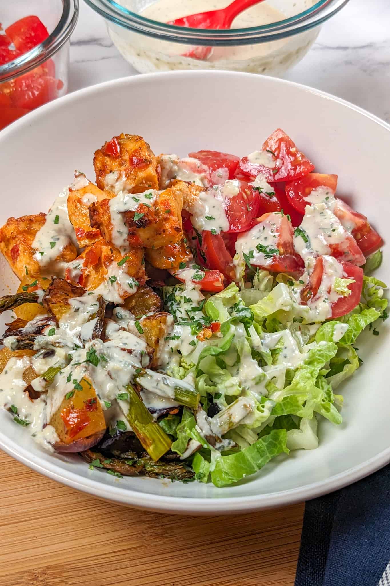 top view of the Air Fryer Calabrian Chili Salmon and Vegetables Bowl in a wide rim bowl, a dish where the cubed baked salmon, quartered campari tomatoes, shredded romaine lettuce and roasted vegetables share equal pie part with the rosemary tahini dressing drizzled in a zig zag on top